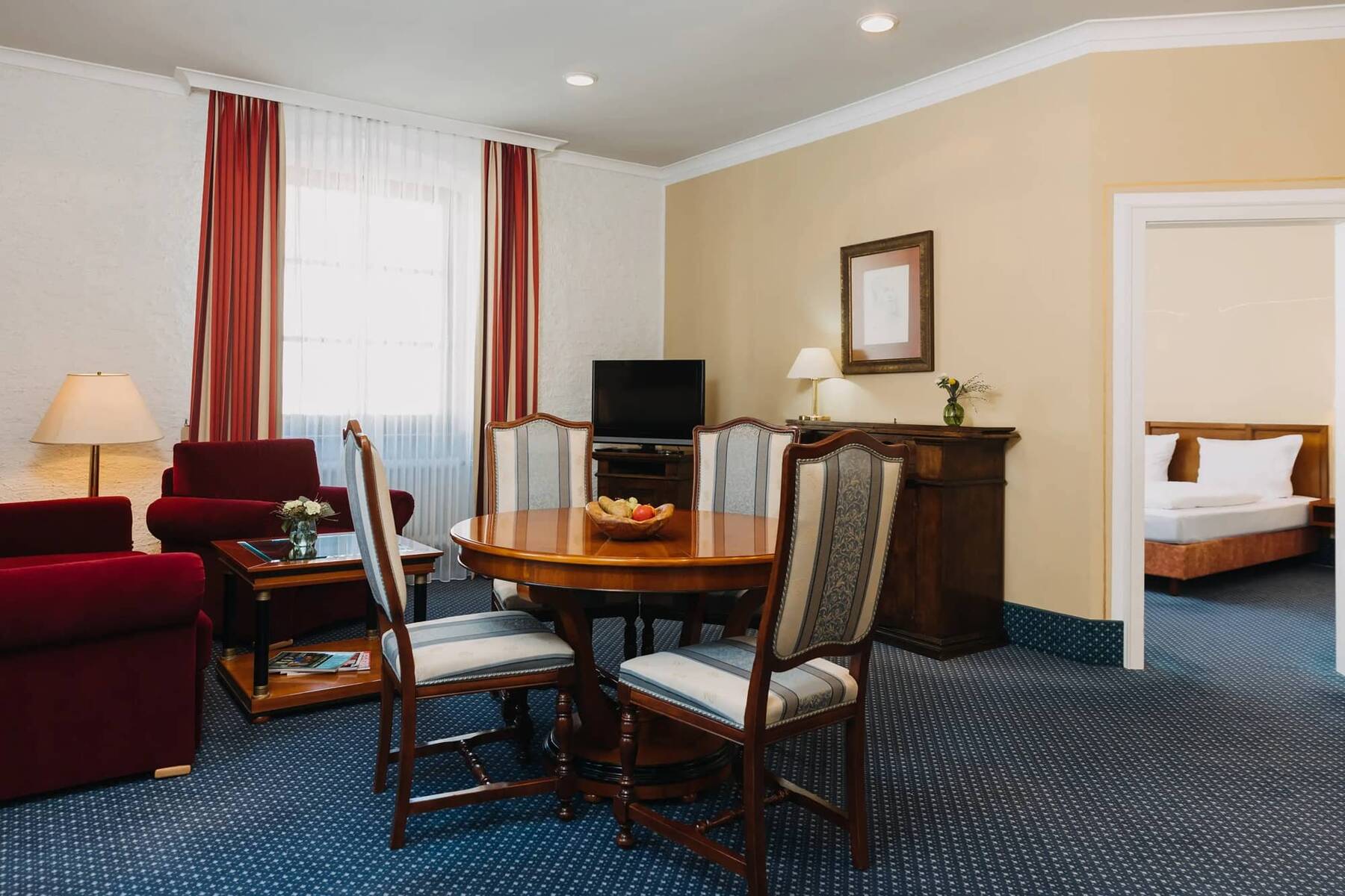 Gemütliches Hotelzimmer im Familienhotel mit einem Essbereich, roten Sofas und einem Fernseher, ideal für einen Familienurlaub.