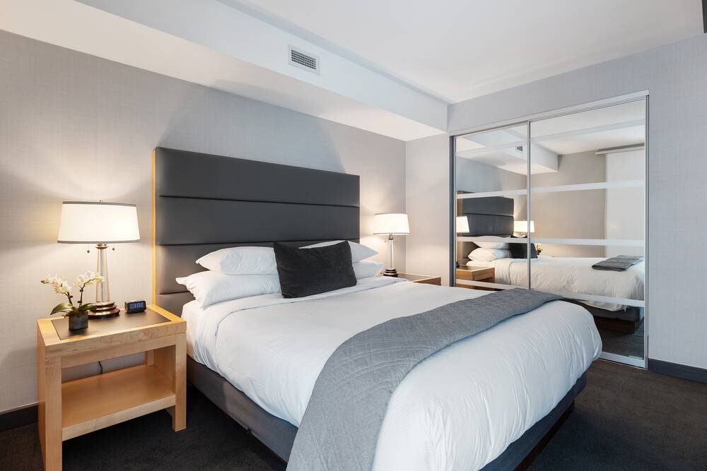 Modernes Schlafzimmer im Hotel mit einem großen Bett, Nachttischlampe und Spiegel, ideal für einen erholsamen Familienurlaub.