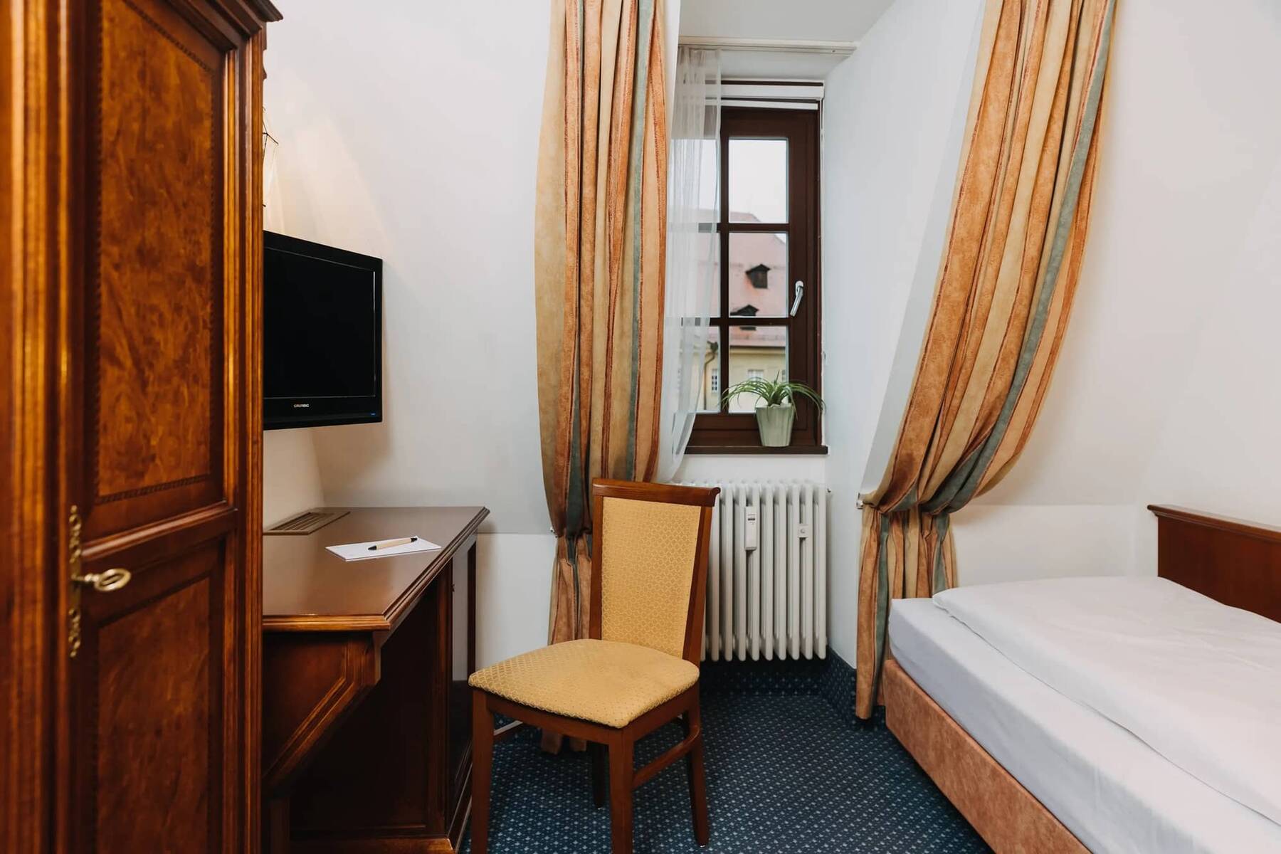 Gemütliches Zimmer im Hotel mit einem Fernseher, einem Schreibtisch und Blick aus dem Fenster, ideal für einen entspannten Aufenthalt.