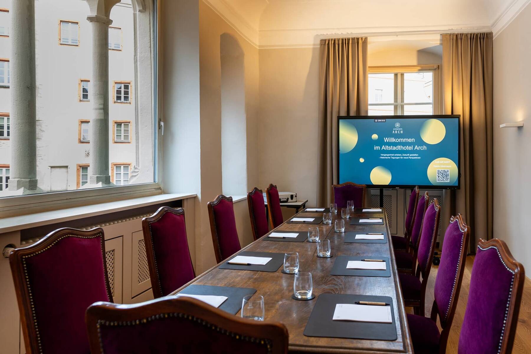 Tagungsraum im Altstadthotel Arch mit stilvollem Holz-Meetingtisch, roten Stühlen und moderner Präsentationstechnik, ideal für Geschäftsveranstaltungen.