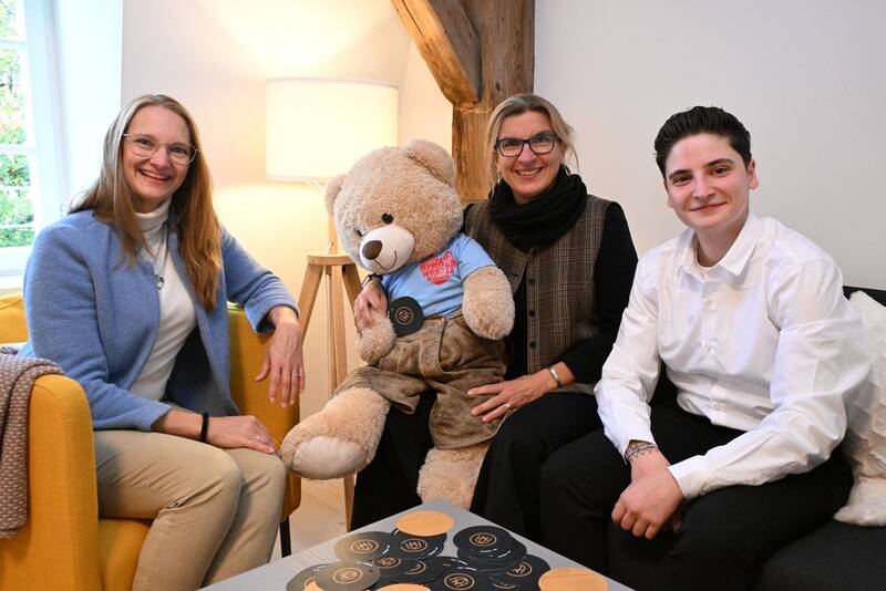 Drei Personen im Hotel sitzen zusammen mit einem großen Kuschelbären auf einem Sofa, ideal für einen Familienurlaub.