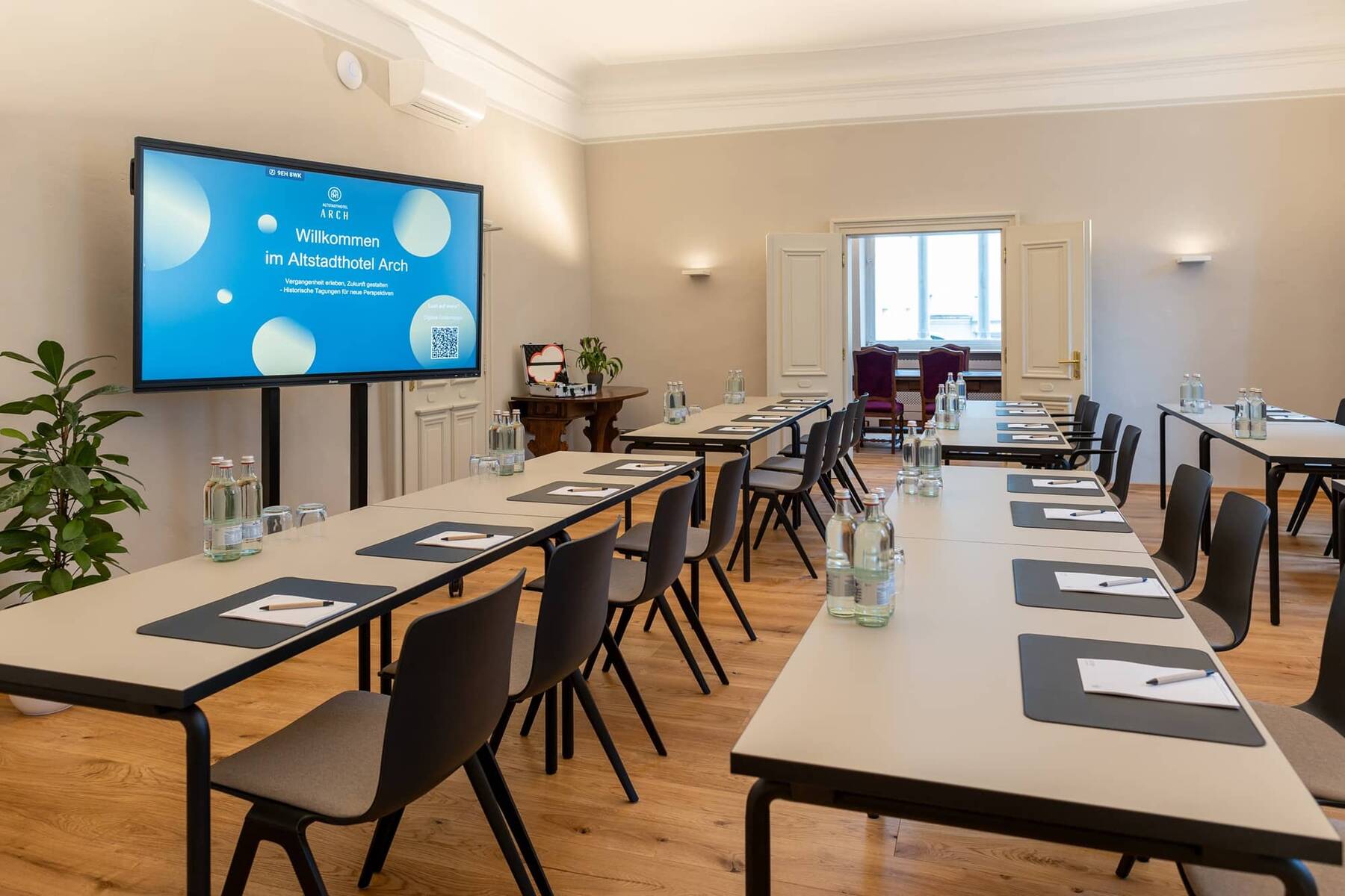 Konferenzraum im Altstadthotel Arch mit Tischen, Stühlen und einem großen Bildschirm, ideal für Geschäftsveranstaltungen in der Stadt.