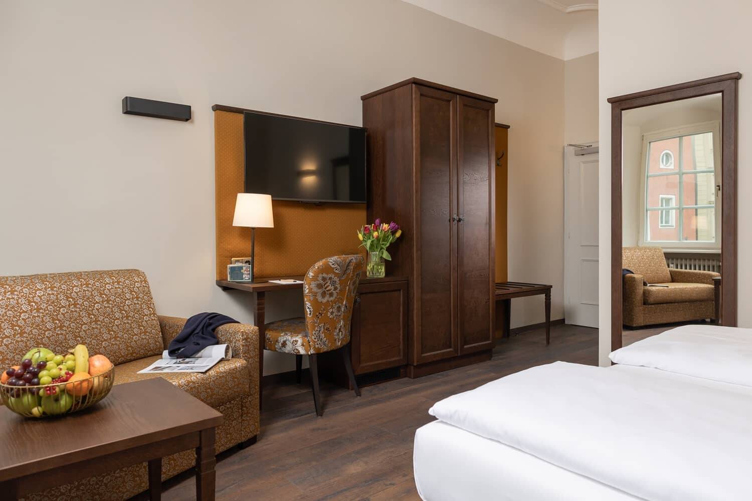 Modernes Hotelzimmer mit Fernseher, Schreibtisch und gemütlicher Sitzecke, ideal für einen entspannten Aufenthalt im Familienurlaub.