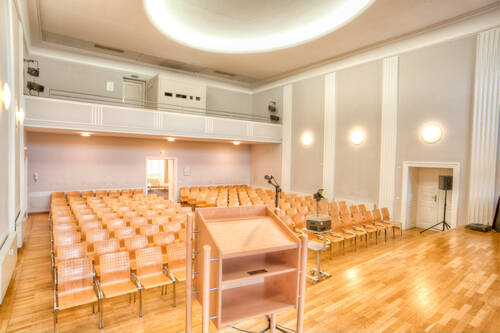Ein Konferenzraum im Eventzentrum mit Holzfußboden, Reihen von Stühlen und einem Podium für Präsentationen und Events.