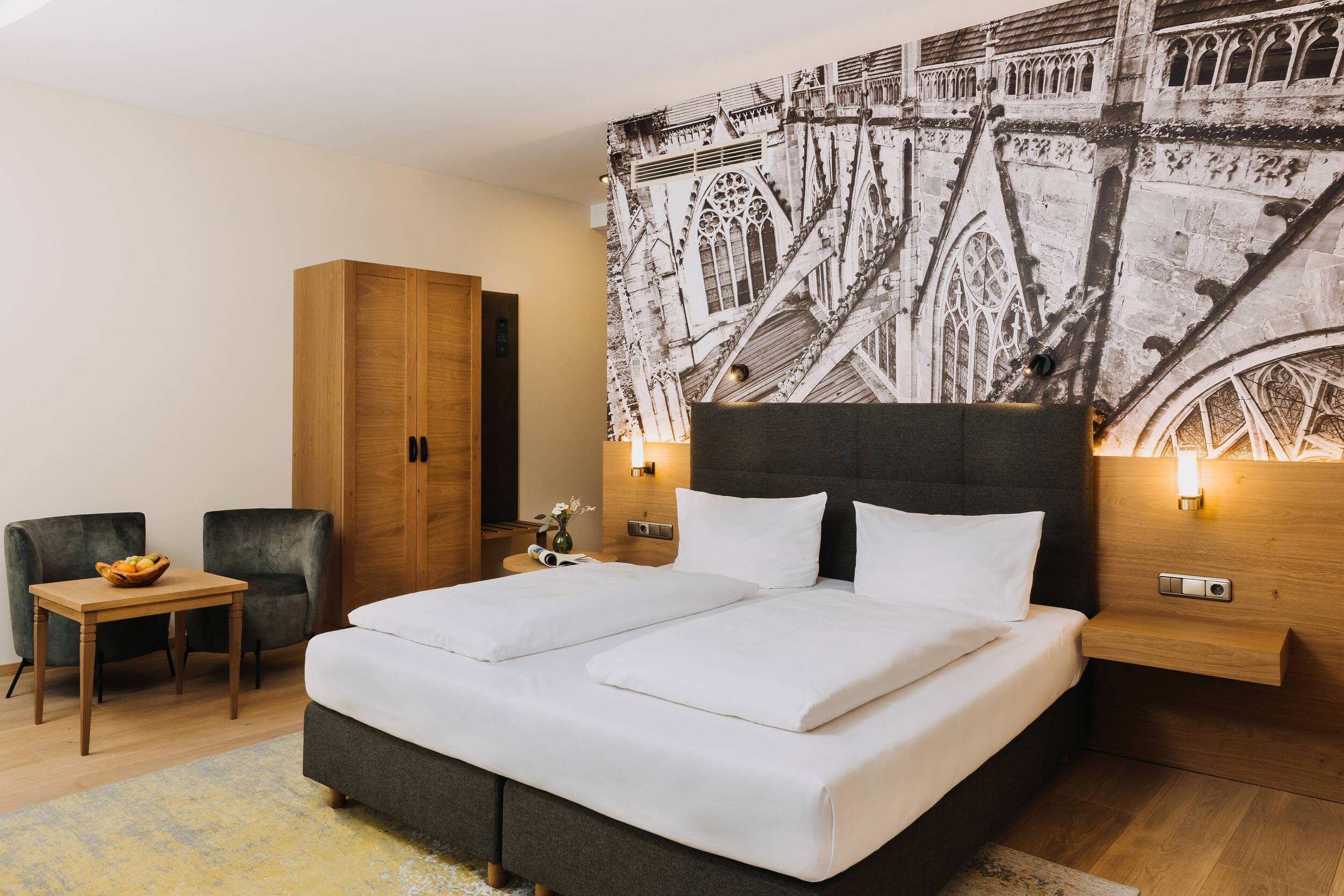 Ein modernes Hotelzimmer mit Doppelbett, Holzschrank und Sitzgelegenheiten, ideal für einen erholsamen Familienurlaub.