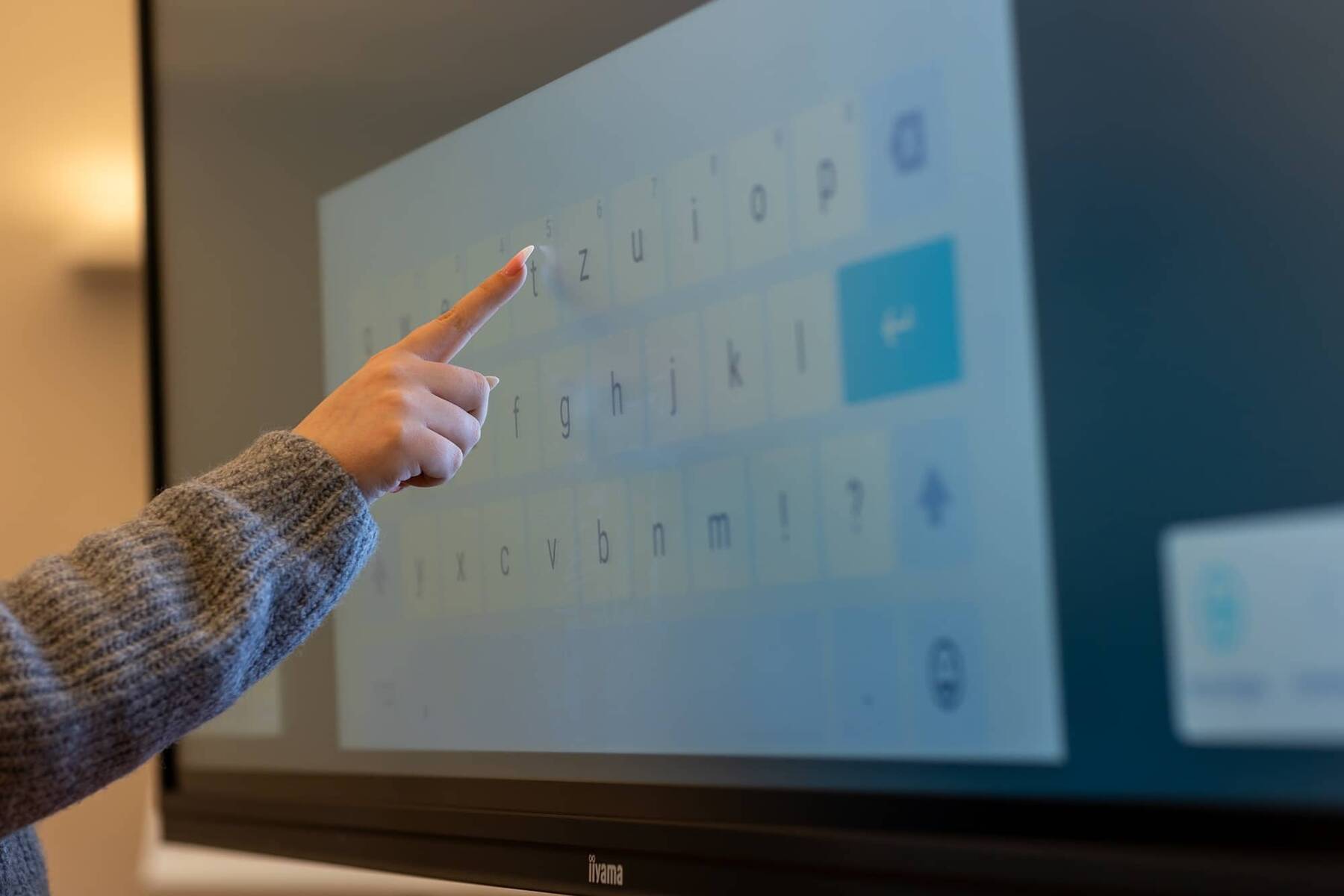 Eine Hand tippt auf ein Touchscreen-Display während einer Präsentation, das für Schulungen und Meetings genutzt wird.