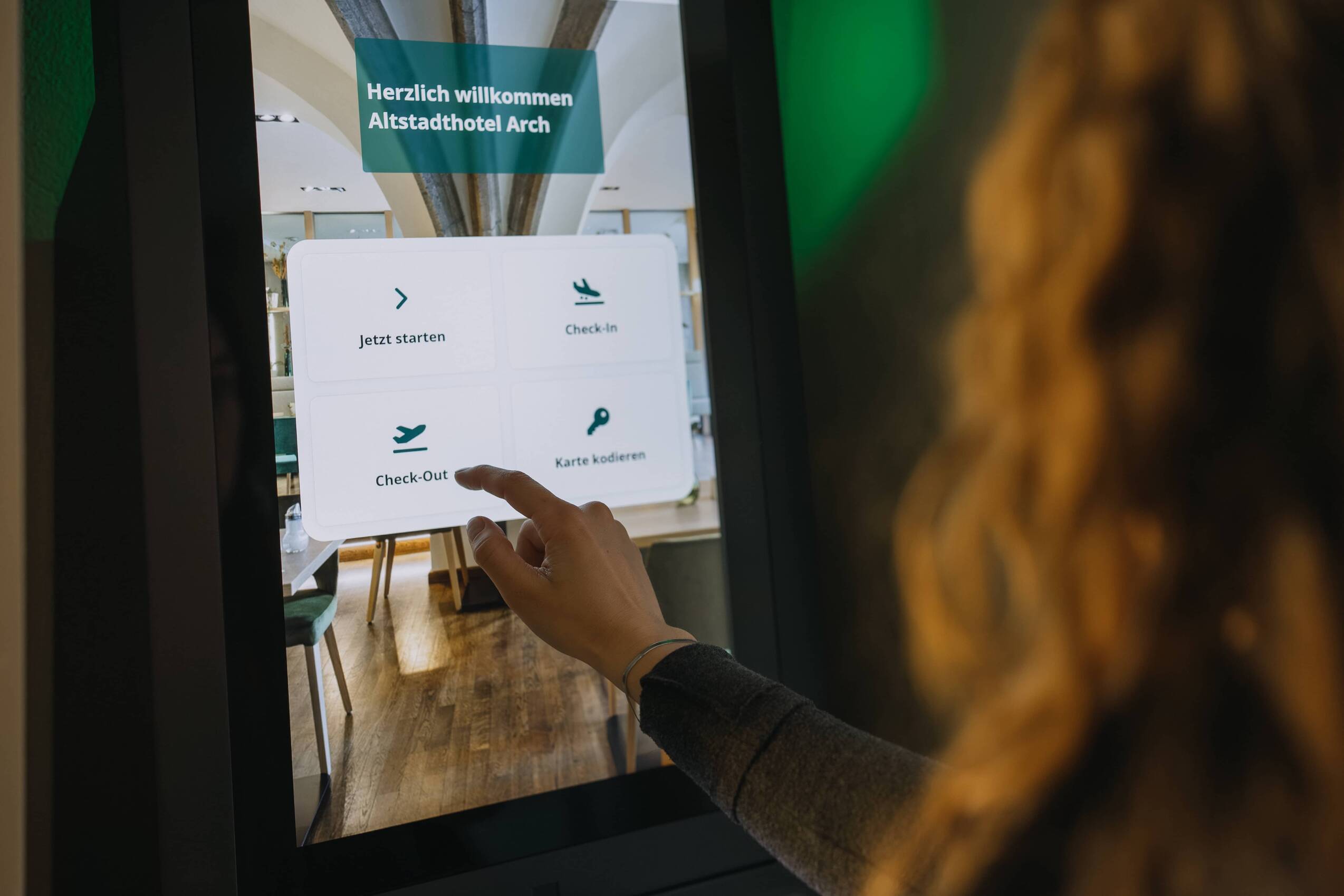 Gast bedient den digitalen Self-Check-in-Automaten im Altstadthotel Arch Regensburg mit den Optionen Check-in, Check-out und Karte kodieren