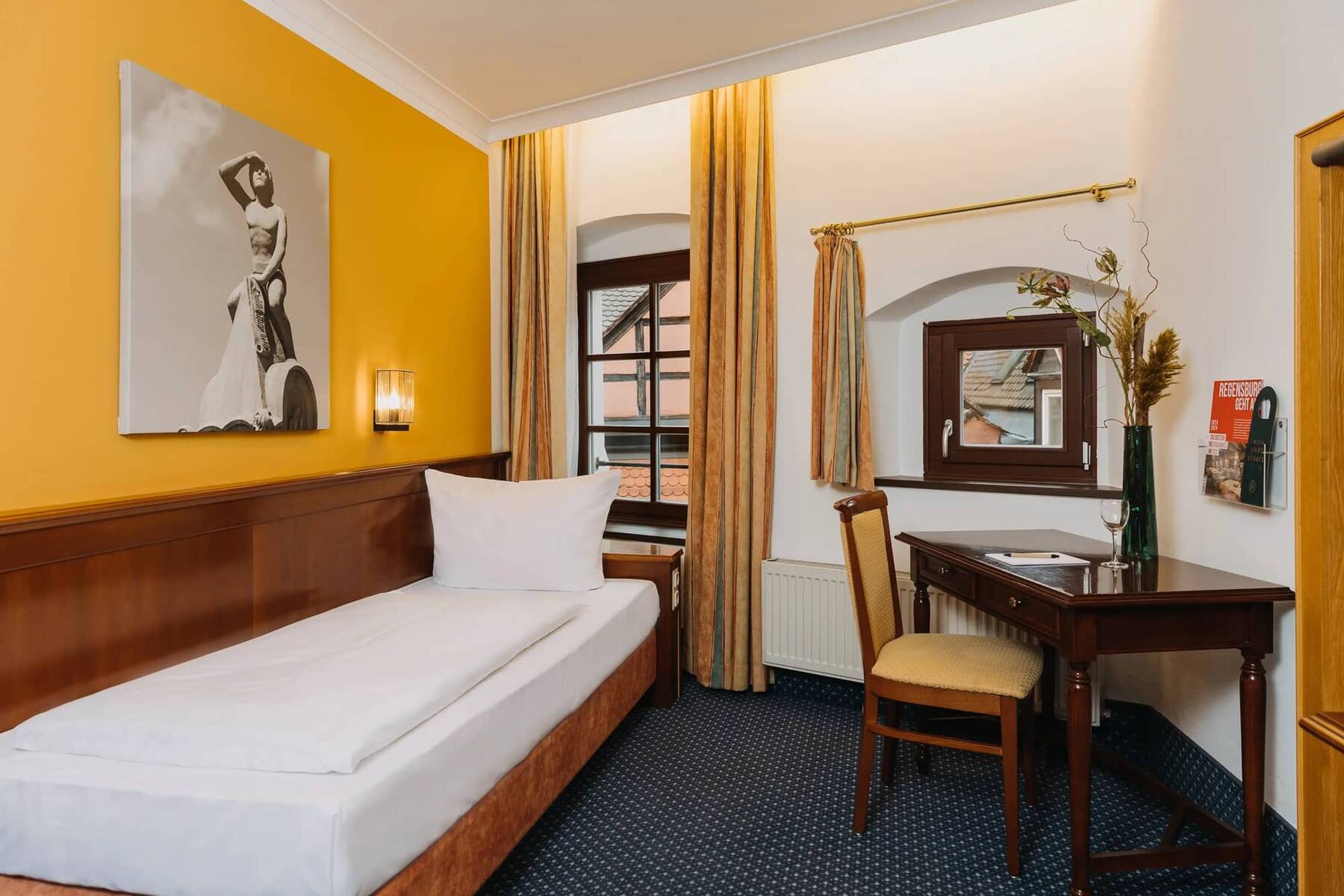 Einzelzimmer im Hotel mit Holzvertäfelung, einem Schreibtisch und einem Fenster mit Blick auf die Altstadt.
