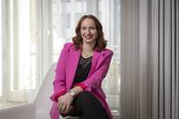 Portrait einer Frau in pinkem Blazer, die in einem hellen Innenraum sitzt, ideal für Business- oder Karriere-Themen.