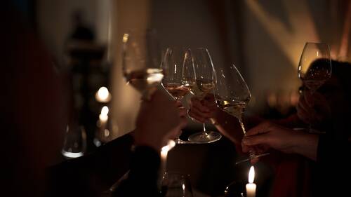 Several guests clinking white wine glasses by candlelight at Maxim's Fine Wine Bar & Tapas, Altstadthotel Arch Regensburg