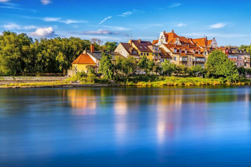 Bunte Häuser am Ufer eines ruhigen Flusses, umgeben von Bäumen und Natur, ideal für einen erholsamen Urlaub.