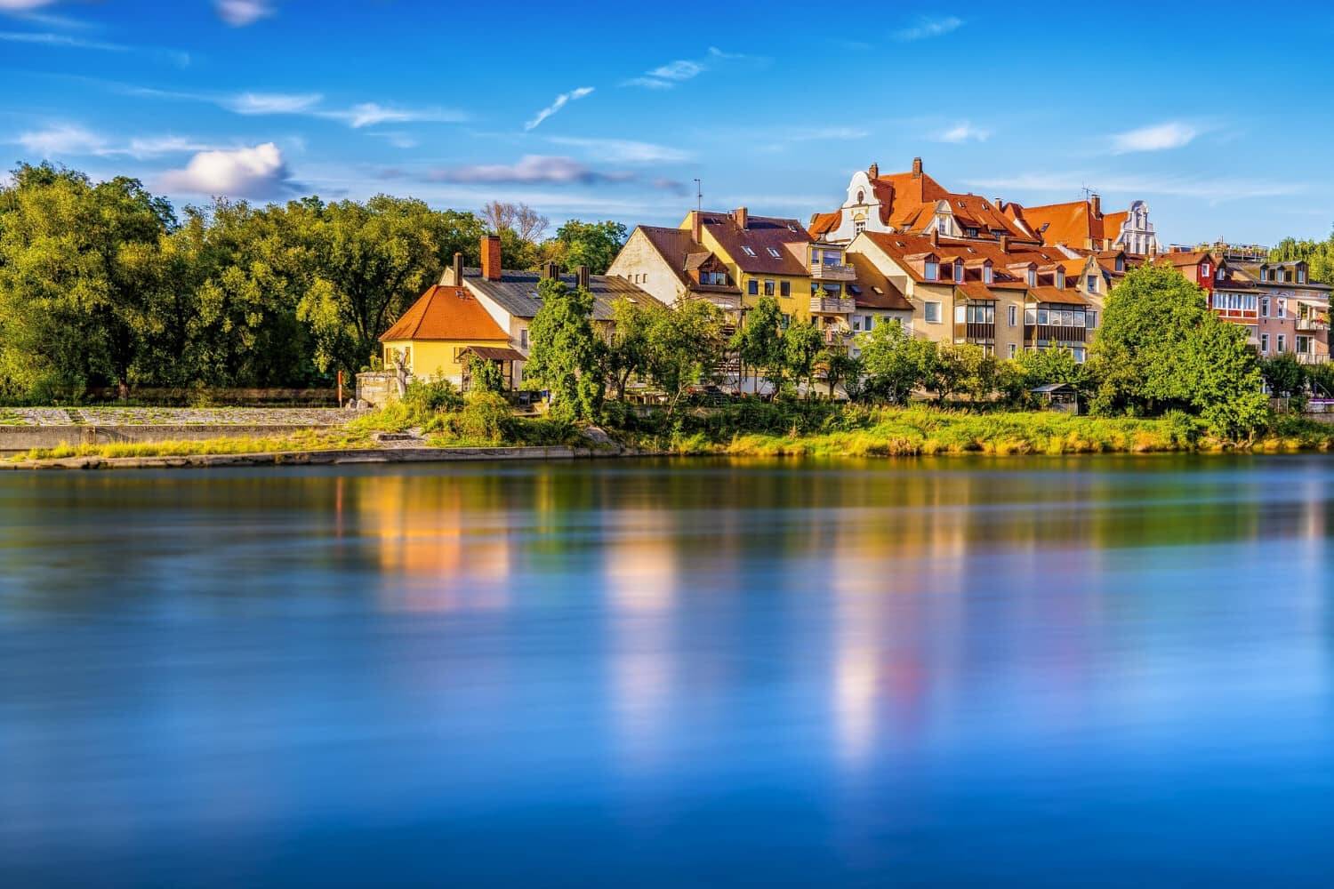 Bunte Häuser am Ufer eines ruhigen Flusses, umgeben von Bäumen und Natur, ideal für einen erholsamen Urlaub.