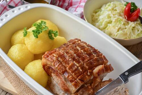Ein traditionelles deutsches Gericht mit knusprigem Schweinebraten, Kartoffelknödeln und frisch zubereitetem Sauerkraut auf einem Teller.