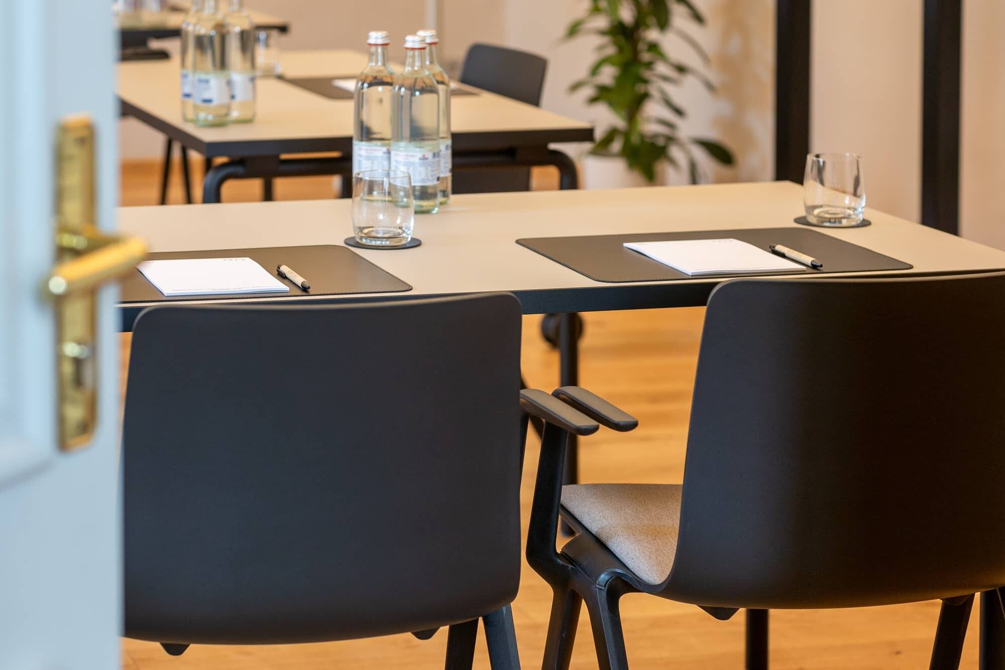 Einblick in einen modernen Konferenzraum im Hotel Alpenglück, ausgestattet mit Tischen, Stühlen, Wasserflaschen und Schreibmaterial für Meetings.