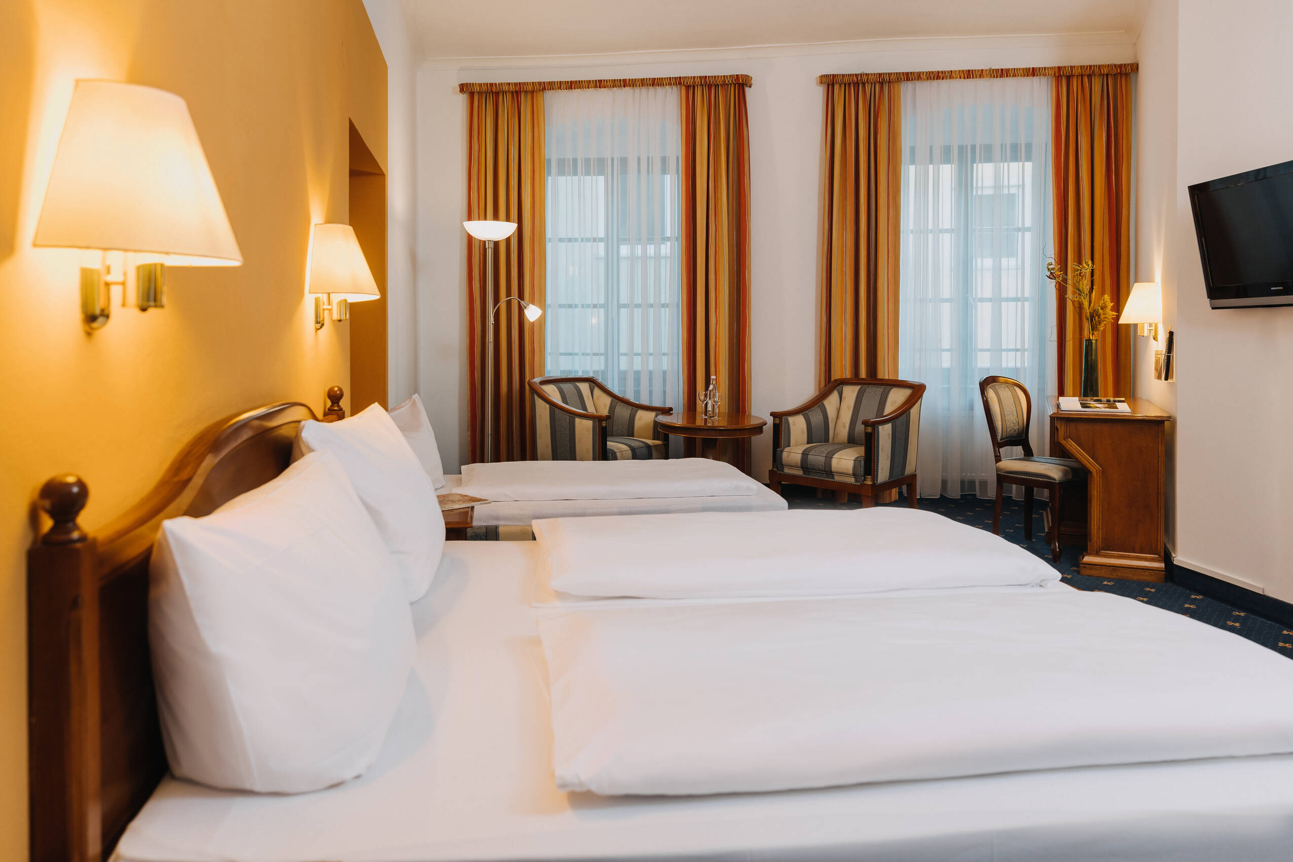 Ein modernes Hotelzimmer mit zwei Betten, gemütlichen Sesseln und Fenster mit Vorhängen, ideal für einen Familienurlaub.