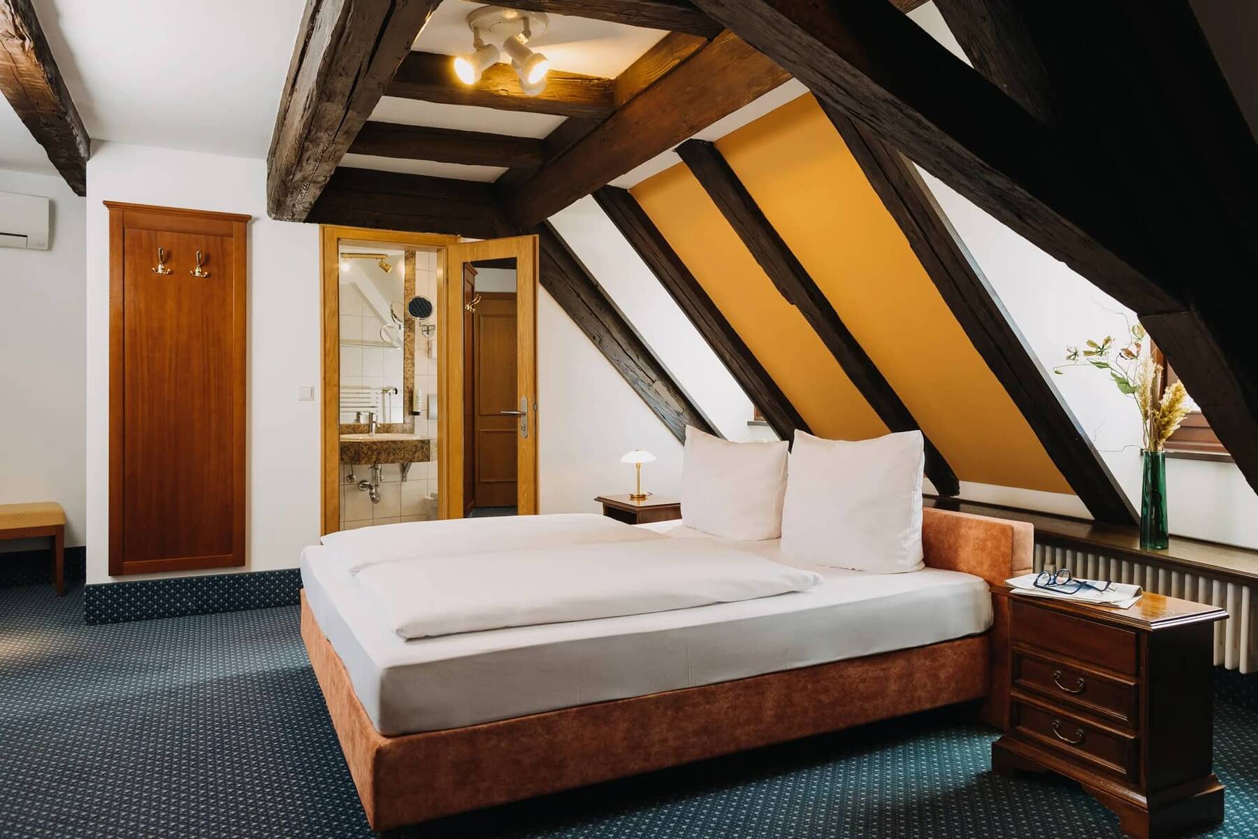 Ein gemütliches Zimmer im Hotel mit schrägen Holzdecken, Doppelbett und modernem Bad, ideal für einen Familienurlaub.