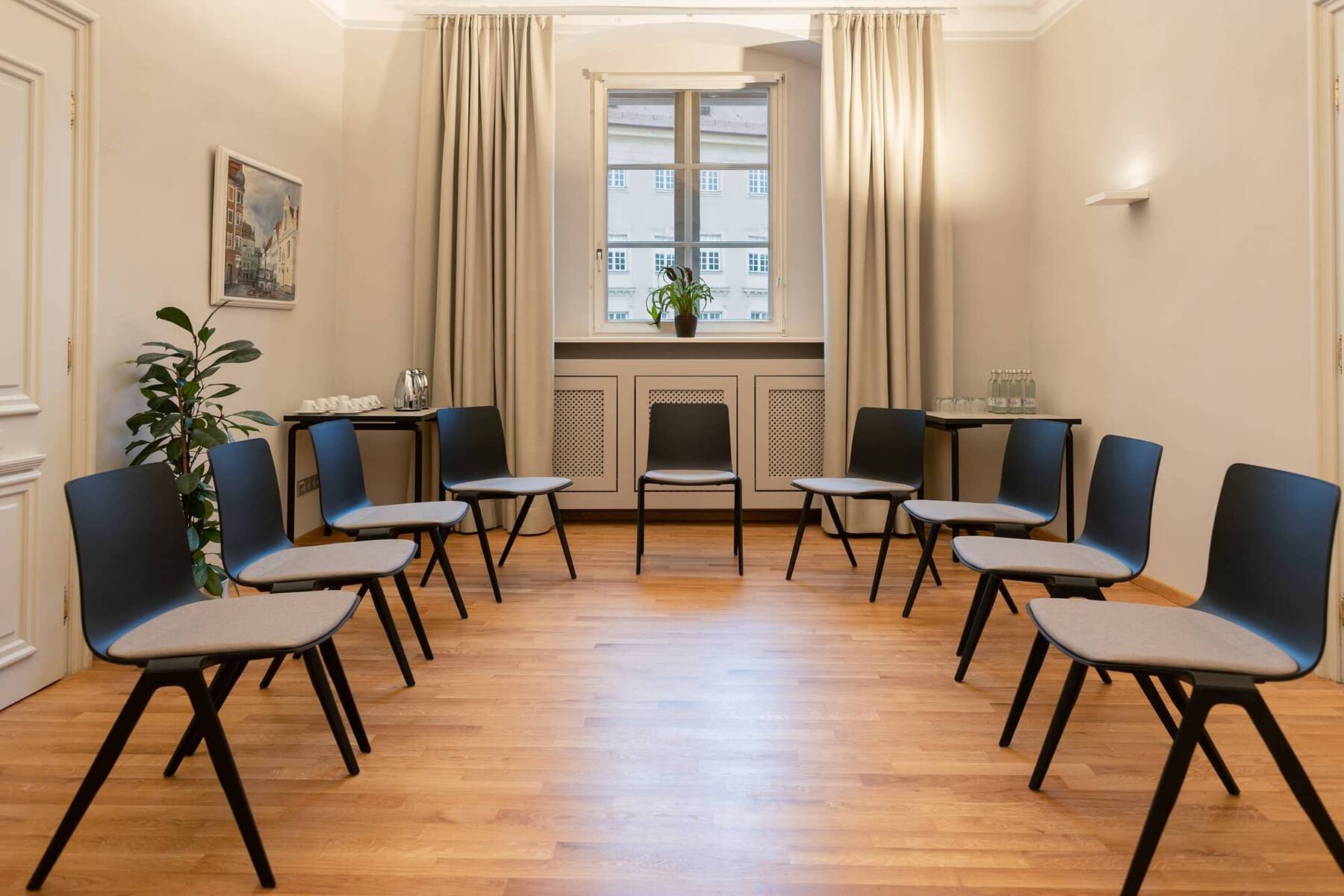 Ein moderner Tagungsraum im Hotel Stadtblick mit schwarzen Stühlen, Holzfußboden und einem Fenster, ideal für Meetings und Schulungen.