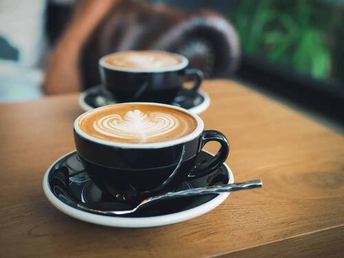 Zwei Tassen Kaffee mit kunstvollem Milchschaum auf einem Holztisch im Café, ideal für eine entspannte Kaffeepause.