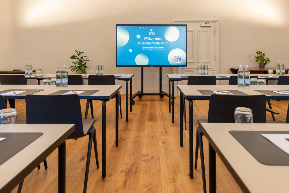 Konferenzraum im Altstadthotel Arch mit Tischen, Stühlen und einem Bildschirm für Besprechungen, ideal für Geschäftstreffen.