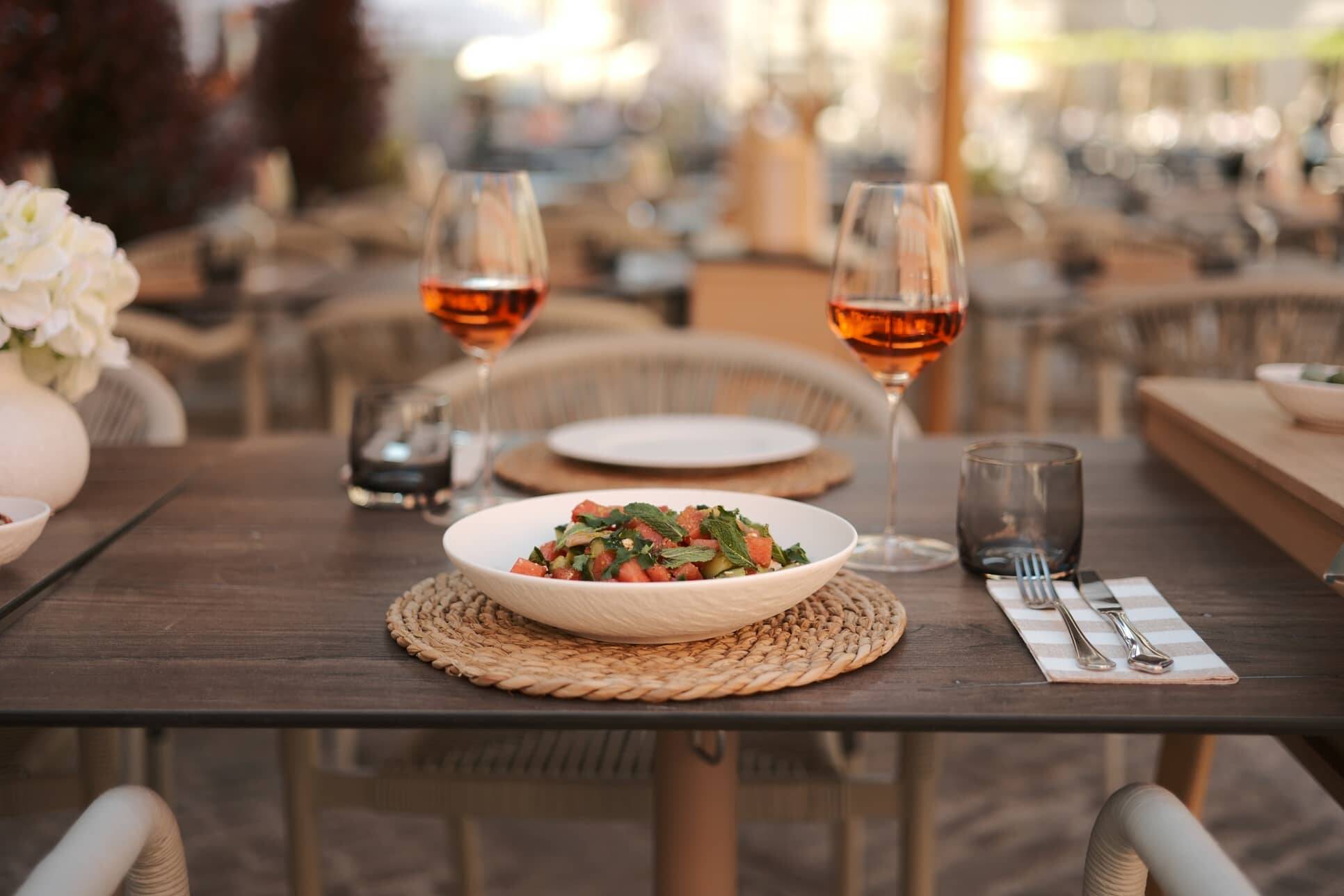 Set table on the outdoor terrace of Maxim's Fine Wine Bar & Tapas at Haidplatz Regensburg with two glasses of rosé wine and a fresh salad