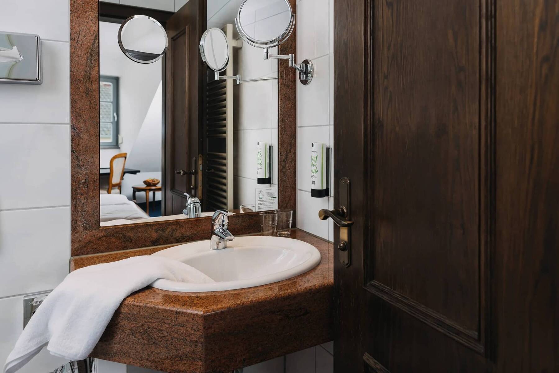 Ein modernes Badezimmer im Hotelzimmer mit einem stilvollen Waschbecken, Spiegel und Handtuch, ideal für einen komfortablen Aufenthalt.
