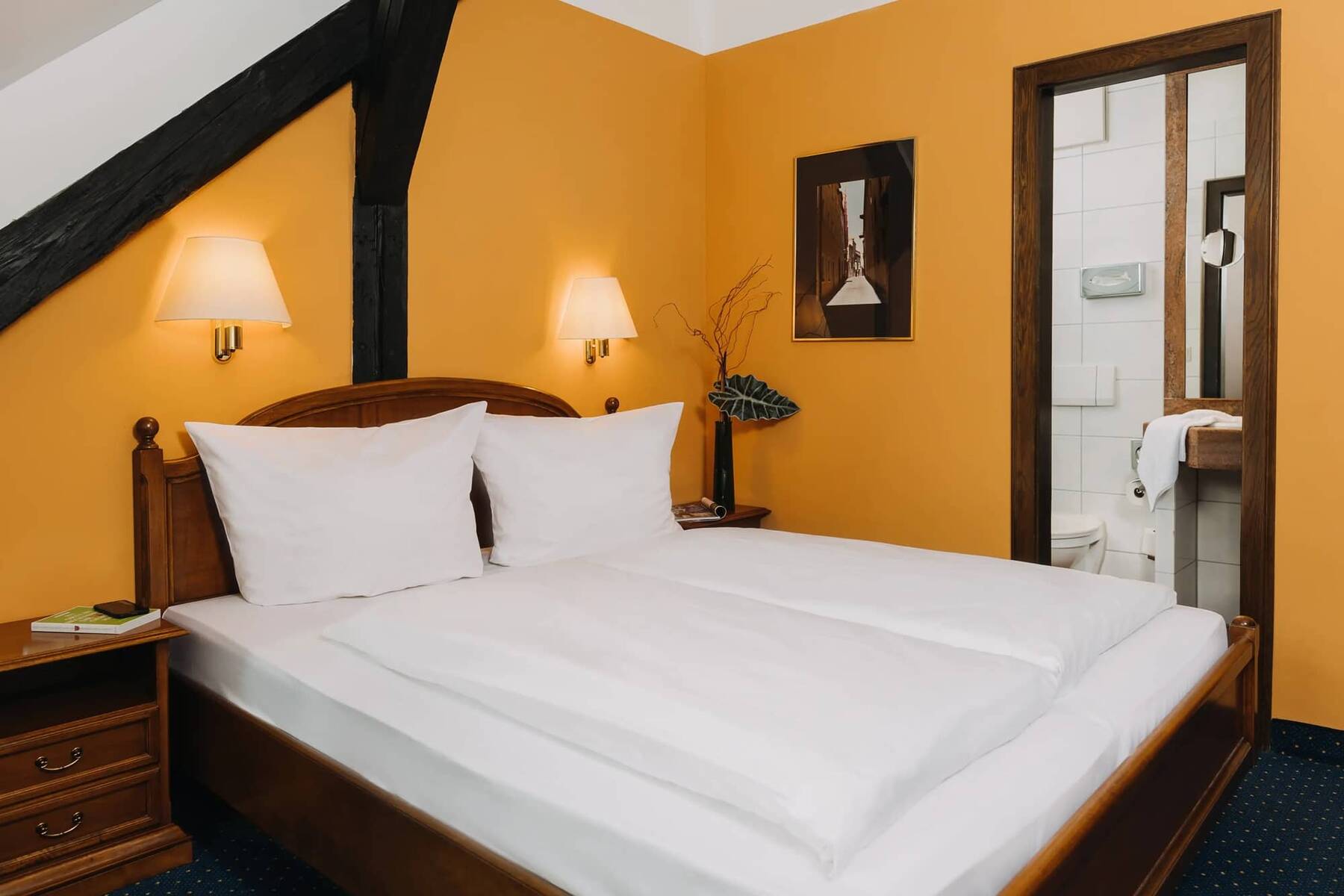Ein gemütliches Zimmer im Hotel mit einem Doppelbett, stilvollen Lampen und einem Blick auf das Badezimmer, ideal für einen entspannten Aufenthalt.