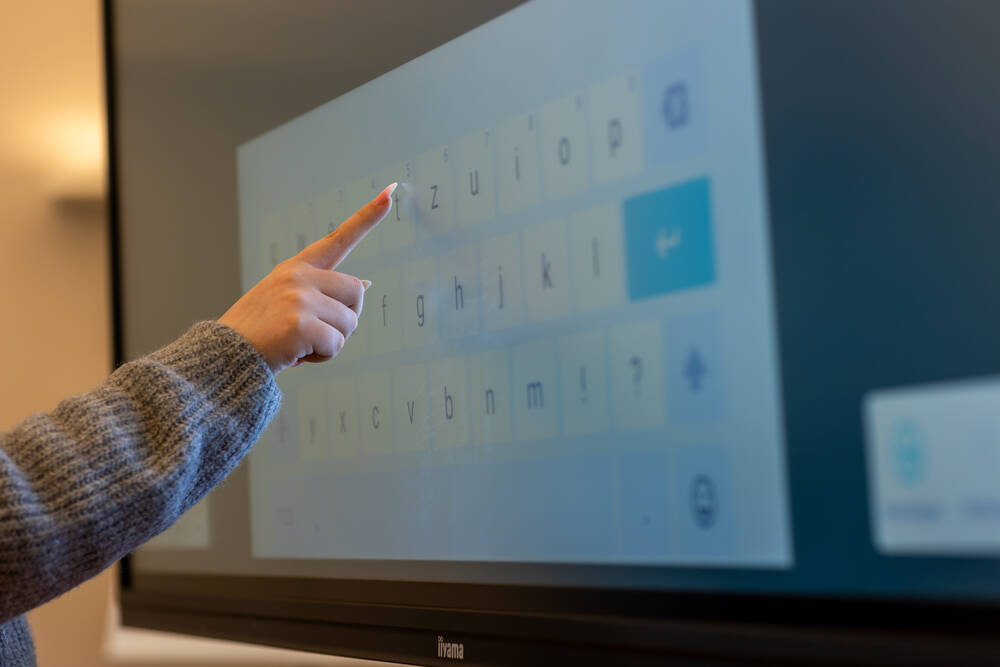 Eine Hand tippt auf die digitale Tastatur eines Touchscreens während einer interaktiven Präsentation in einem modernen Raum.