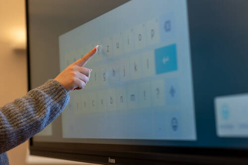 Eine Hand tippt auf die digitale Tastatur eines Touchscreens während einer interaktiven Präsentation in einem modernen Raum.