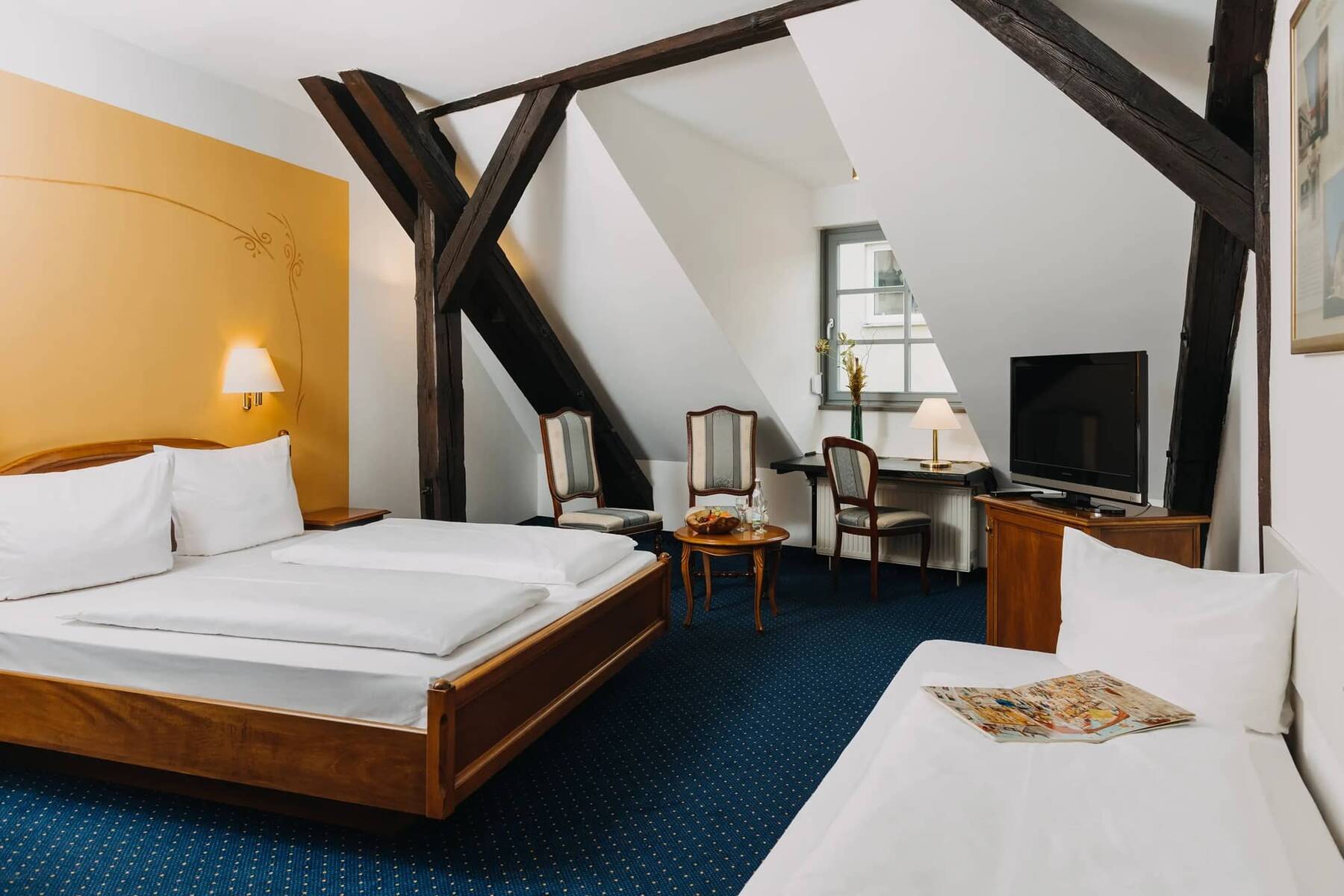 Gemütliches Zimmer im Hotel mit Holzmöbeln, einem Doppelbett und einer Sitzecke, ideal für einen erholsamen Familienurlaub.