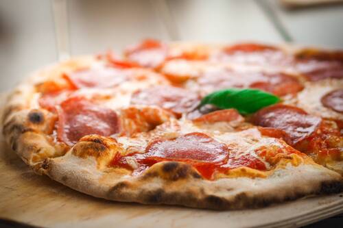 Nahaufnahme einer Pizza mit Salami und Basilikum auf einem Holzbrett, ideal für italienische Küche und Feinschmecker.