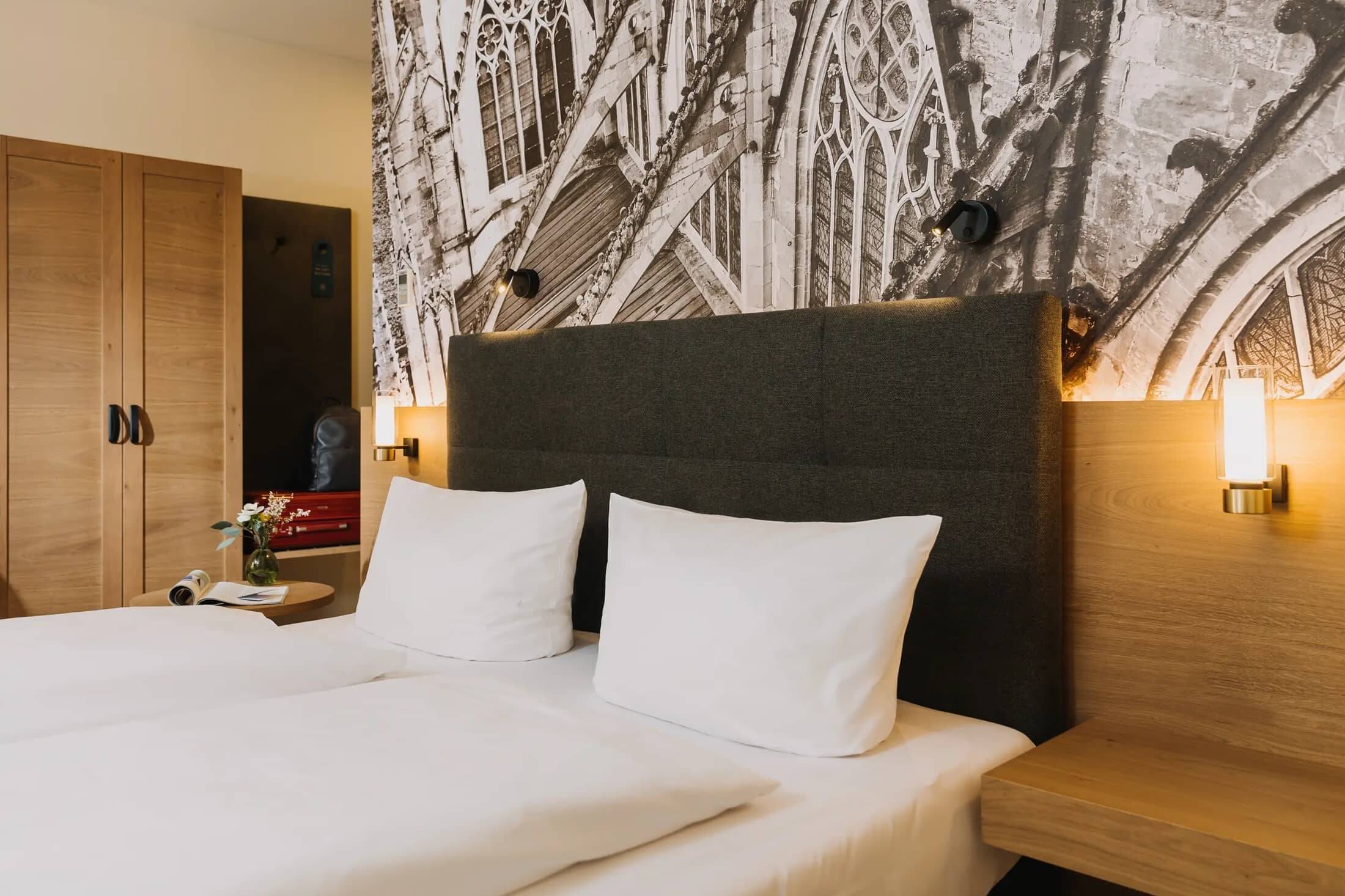 Gemütliches Doppelzimmer im Hotel mit modernem Design, einem großen Bett, stilvollen Lampen und einem dekorativen Wandbild.