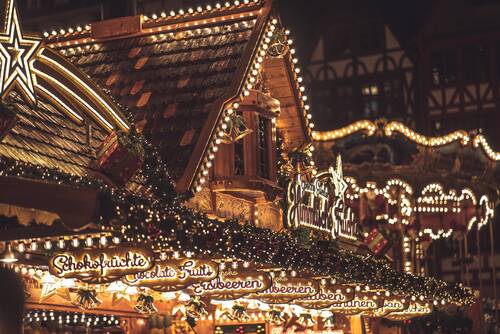 Weihnachtlicher Stand auf einem Weihnachtsmarkt, dekoriert mit Lichtern und Angeboten von Schokoladenfrüchten und Erdbeeren.