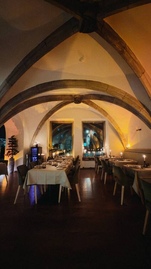 Atmospherically lit vaulted dining room of Maxim's Fine Wine Bar & Tapas at Altstadthotel Arch Regensburg with set tables and candlelight in the evening