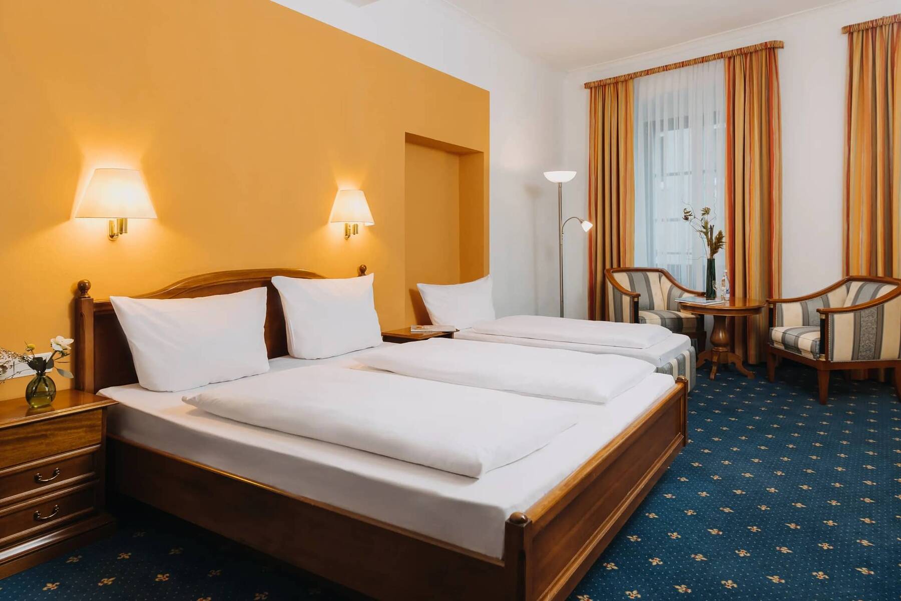 Doppelzimmer im Hotel mit zwei Betten, gemütlichen Sesseln und warmen Farbtönen, ideal für einen erholsamen Aufenthalt.