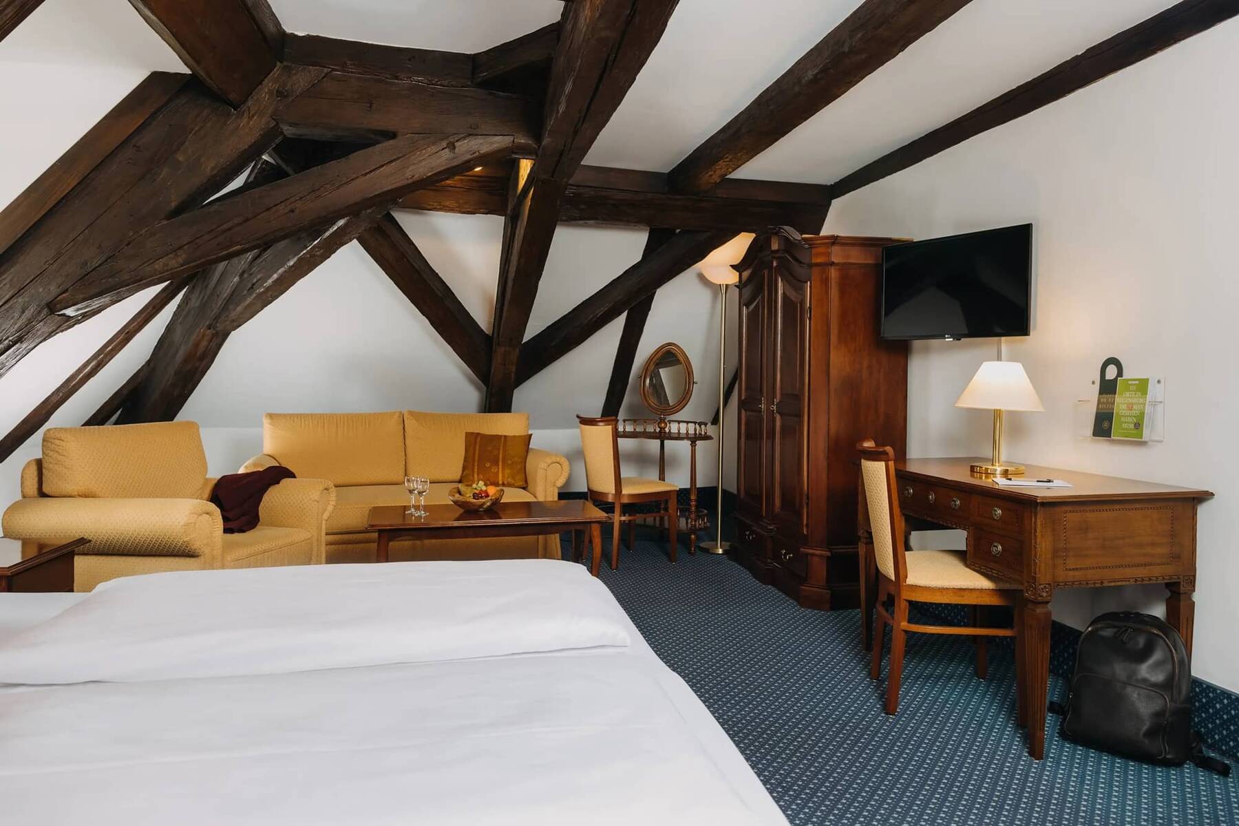 Behagliches Zimmer im Hotel mit Holzdecken, einem Sofa, Schreibtisch und TV, ideal für einen Familienurlaub oder Kurztrip.