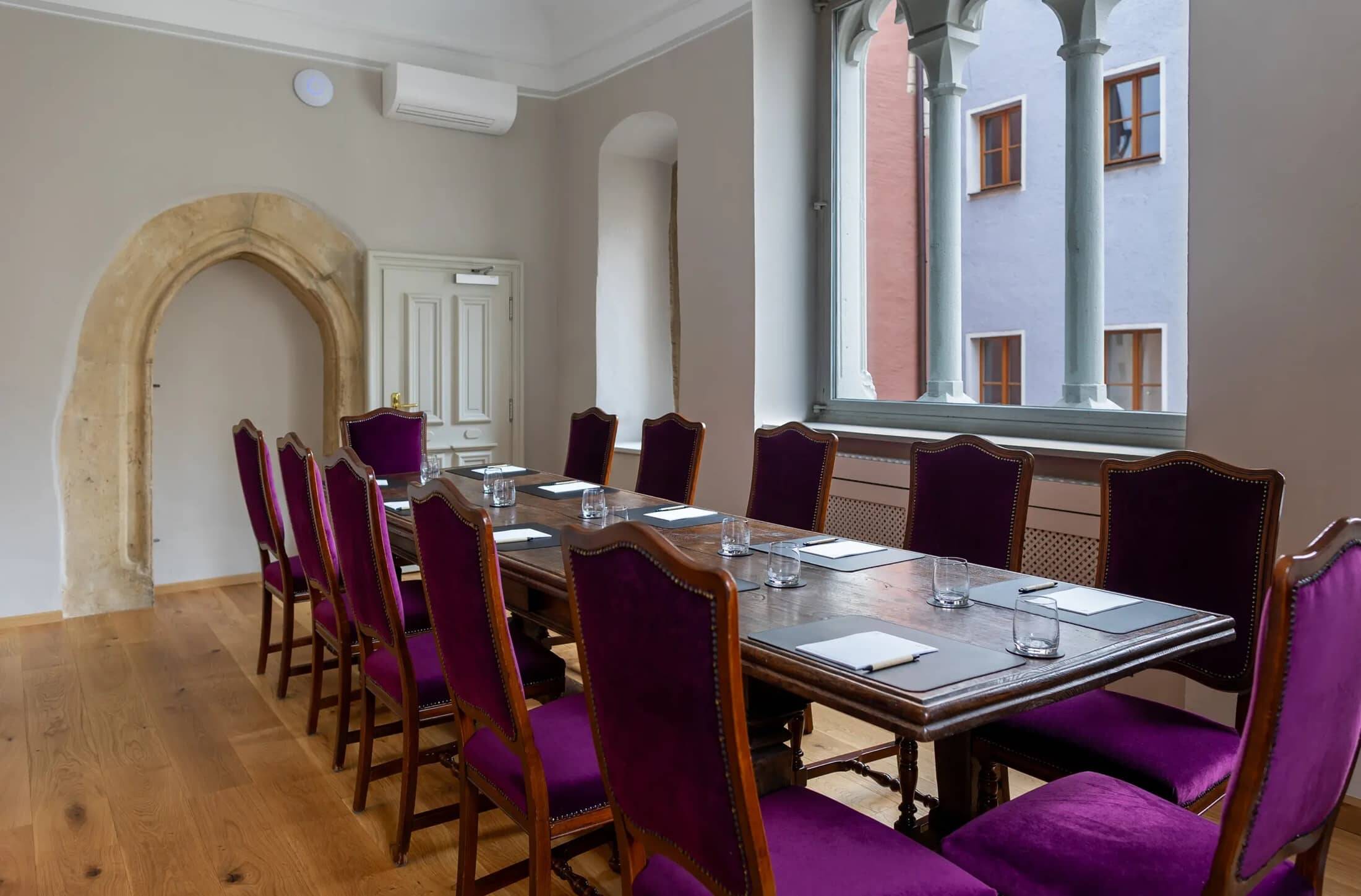 Eleganter Tagungsraum im Hotel mit lila gepolsterten Stühlen und einem großen Tisch, ideal für Meetings und Konferenzen.