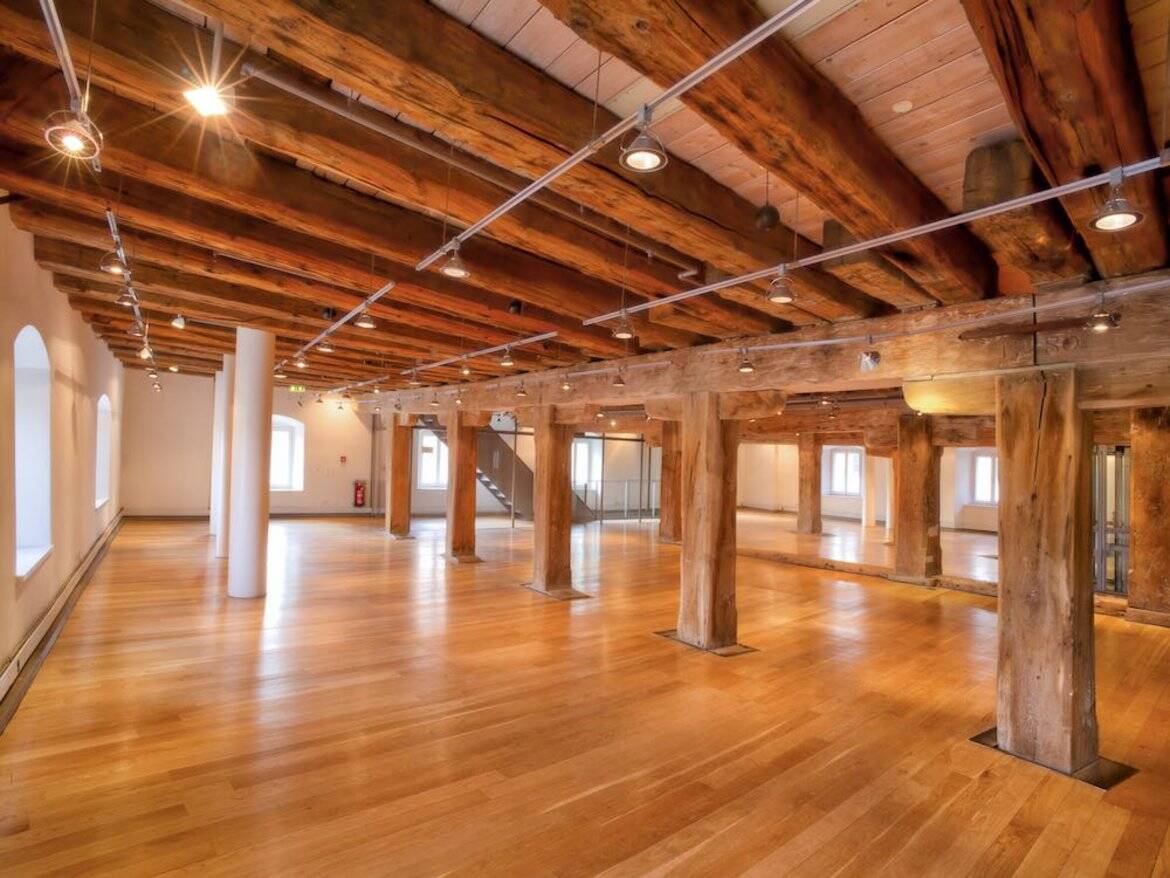 Großer, heller Veranstaltungsraum mit Holzdecken und Säulen, ideal für Events und Feiern in einer modernen Location.