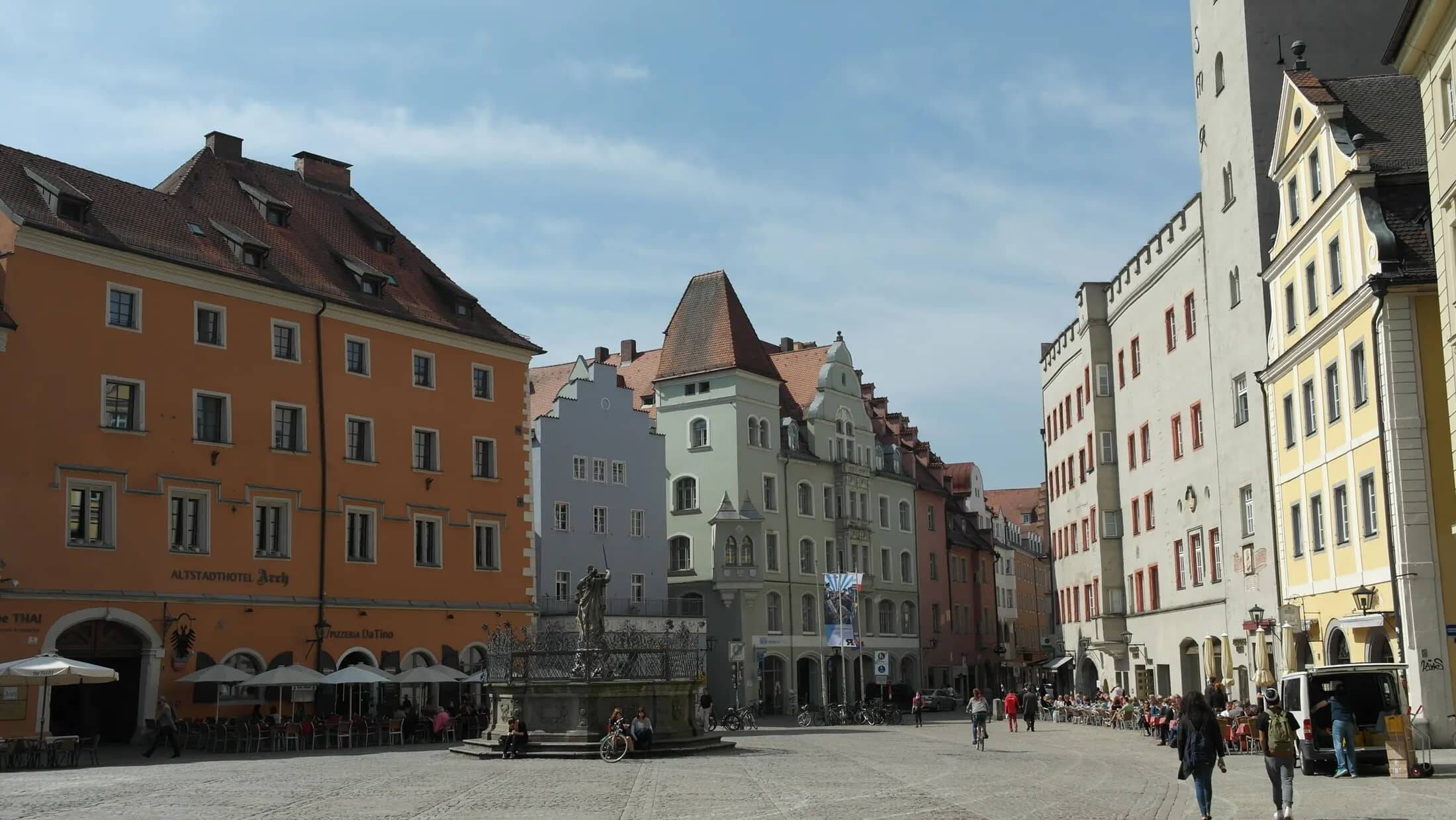 Blick auf eine lebhafte Altstadt mit historischen Gebäuden, Straßencafés und Radfahrern, ideal für einen Städtetrip.