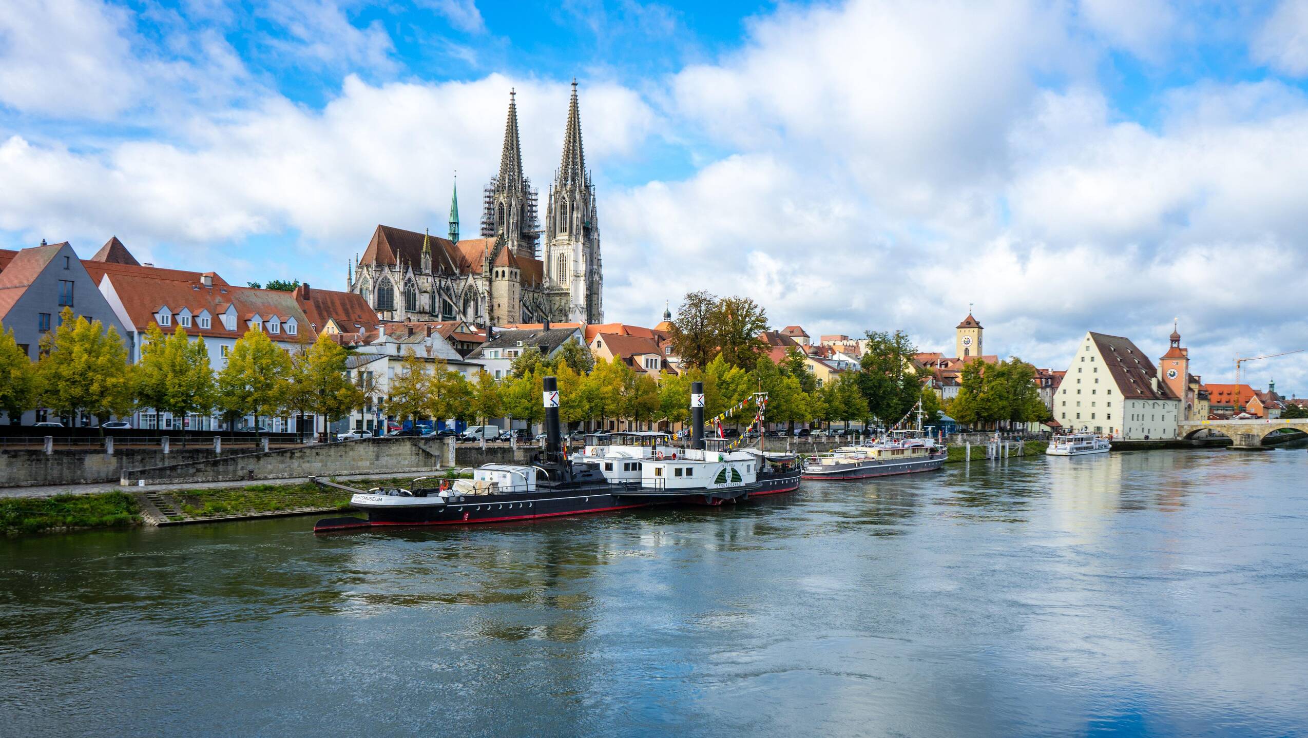 Blick auf die Donau in Regensburg mit historischen Gebäuden und Booten, ideal für einen Familienurlaub in Bayern.