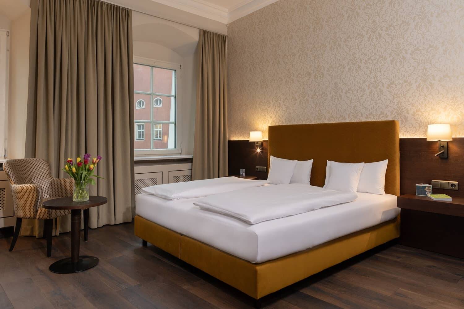 Ein stilvolles Doppelzimmer im Hotel mit einem bequemen Bett, gemütlicher Sitzecke und einer Vase mit bunten Tulpen.
