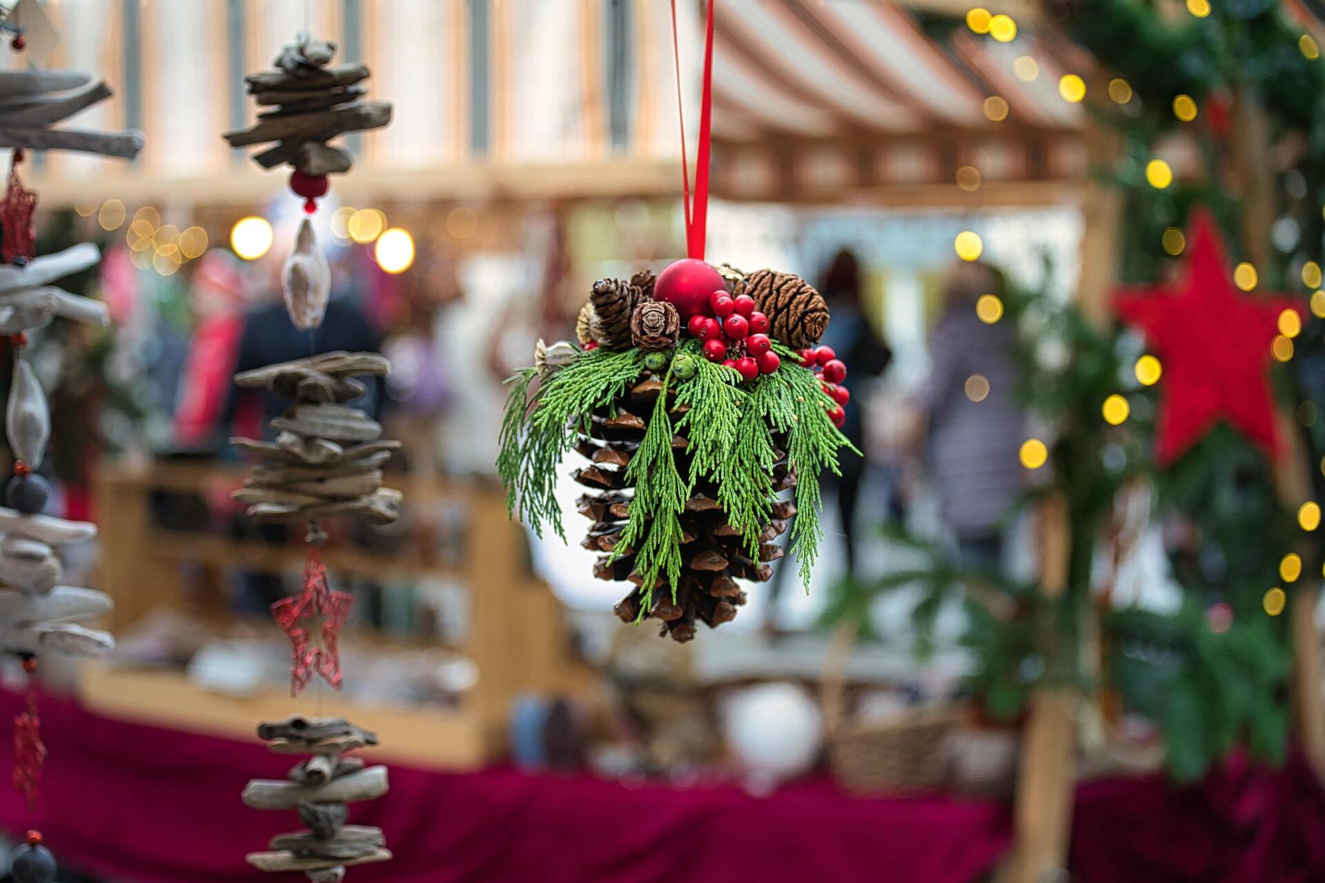 Weihnachtliche Dekoration aus Tannenzapfen und roten Beeren auf einem festlichen Markt, umgeben von Weihnachtsstimmung und Lichtern.
