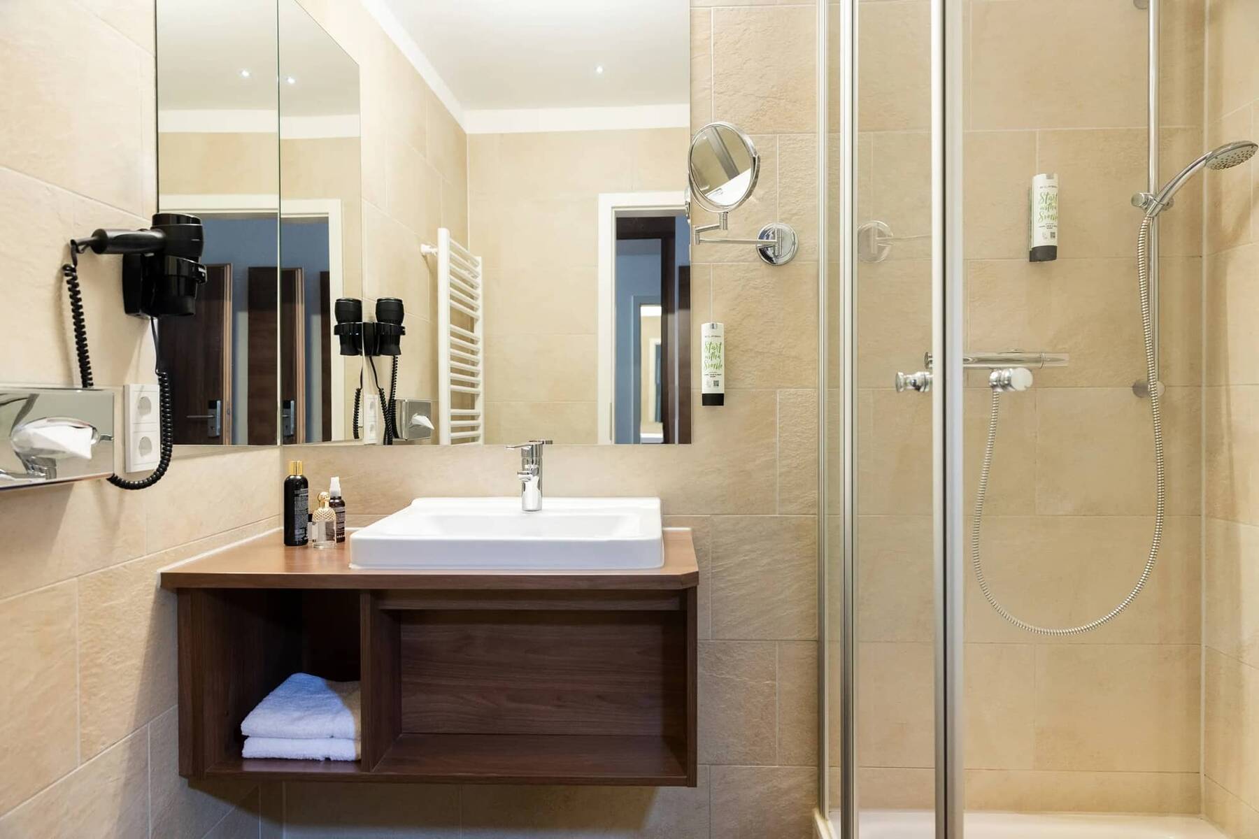 Das moderne Badezimmer im Hotel mit Waschbecken, Dusche und Spiegel, ideal für einen entspannenden Familienurlaub.