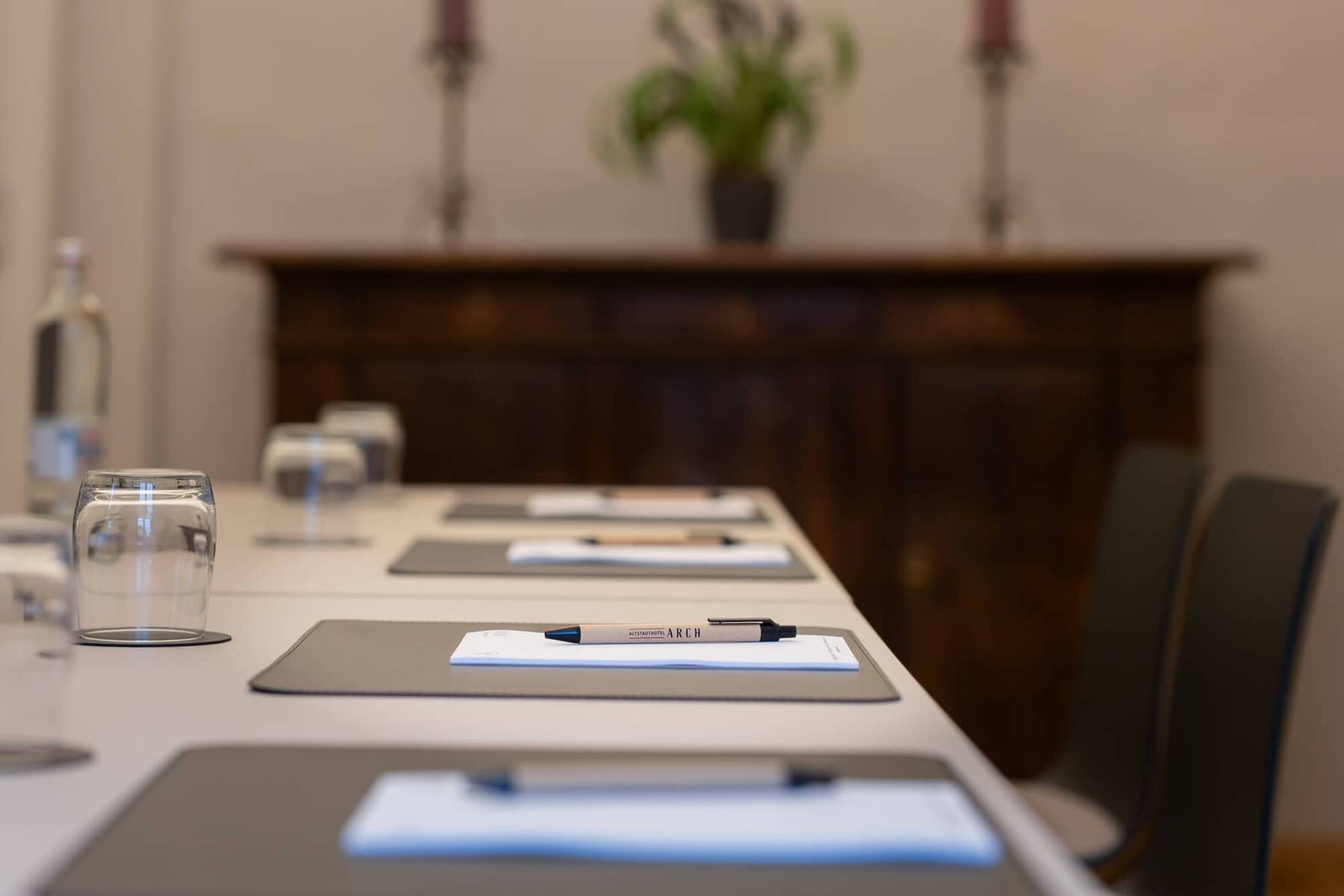 Tagungsraum im Hotel mit einem langen Tisch, Schreibmaterialien und Wasser, ideal für Meetings und Seminare.