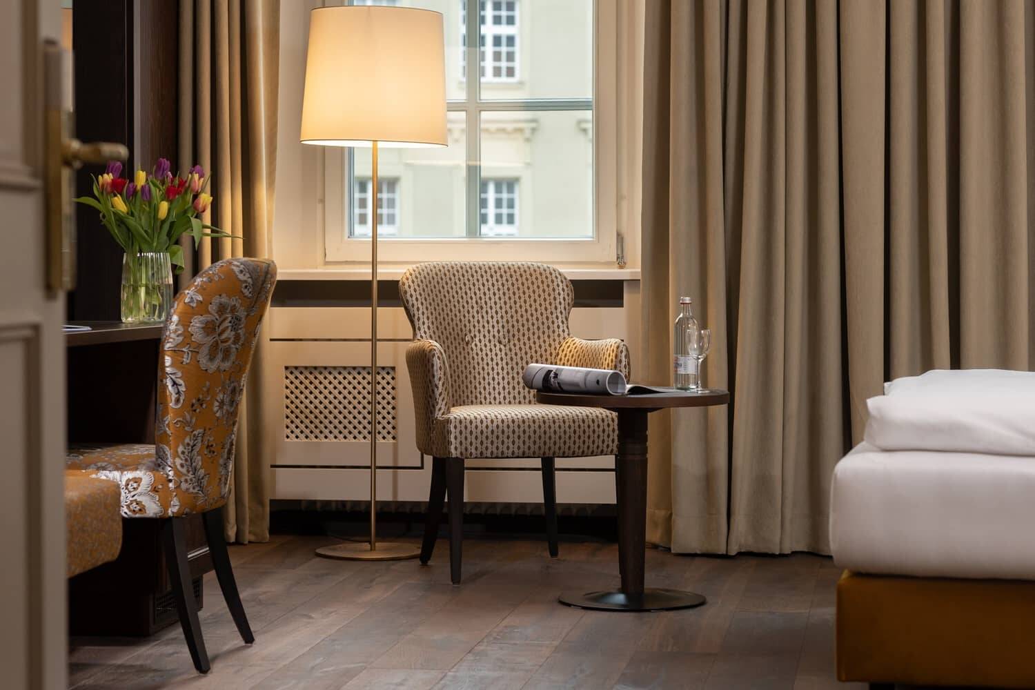 Gemütliche Sitzecke im Hotelzimmer mit Leselampe, Blumenvase und Blick auf die Stadt im Familienhotel.