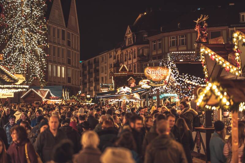 Belebter Weihnachtsmarkt mit stimmungsvoller Beleuchtung, umgeben von Menschen, die die festliche Atmosphäre genießen.