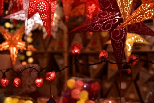 Beleuchtete Papiersterne und eine Lichterkette mit roten Blumen auf einem festlichen Markt, ideal für die Weihnachtszeit.