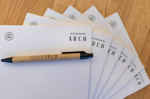Notizblock und Kugelschreiber des Altstadthotels ARCH auf einem Holztisch, ideal für Notizen während des Aufenthalts.