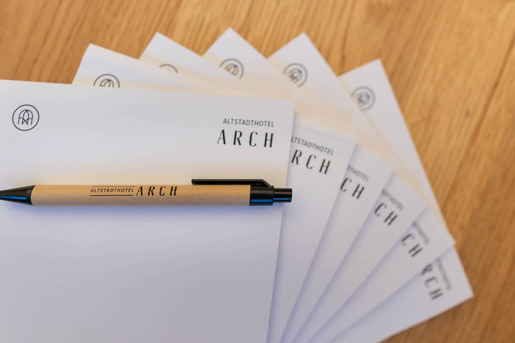 Notizblätter und ein Stift des Altstadthotels ARCH auf einem Holzuntergrund, ideal für Ihre Gedanken im Urlaub.