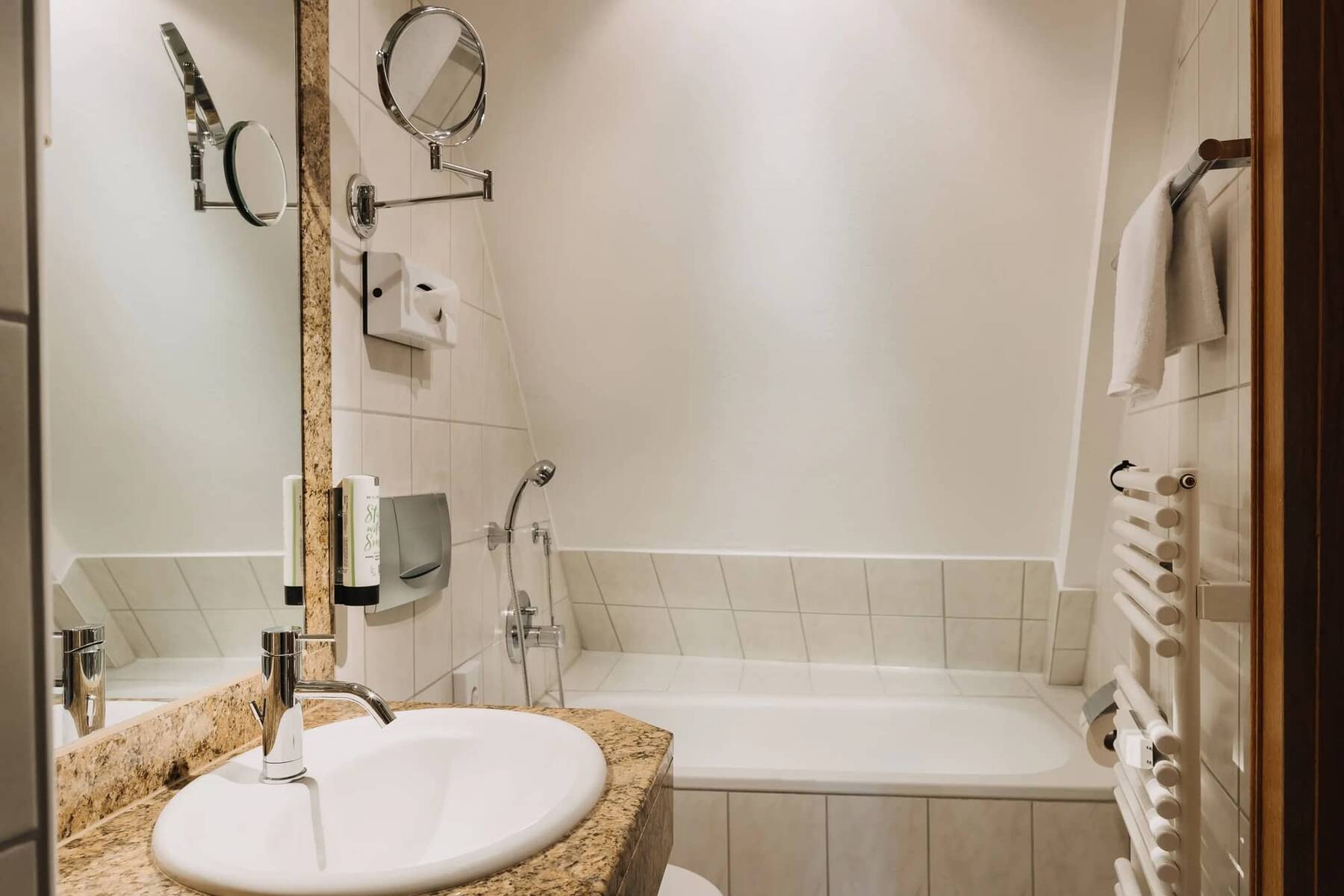 Modernes Badezimmer im Hotel Alpenglück mit Waschbecken, Badewanne und Handtuchwärmer, ideal für einen entspannenden Aufenthalt.