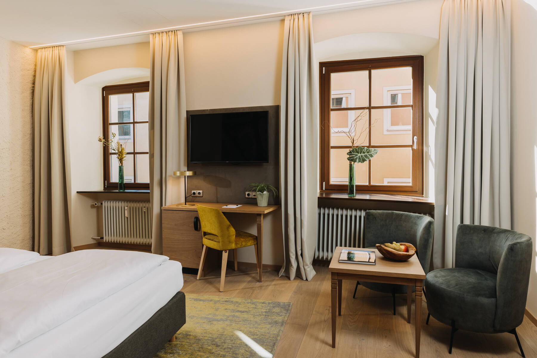 Helles Zimmer im Hotel mit einem Doppelbett, Schreibtisch und zwei Sesseln, ideal für einen entspannten Familienurlaub.